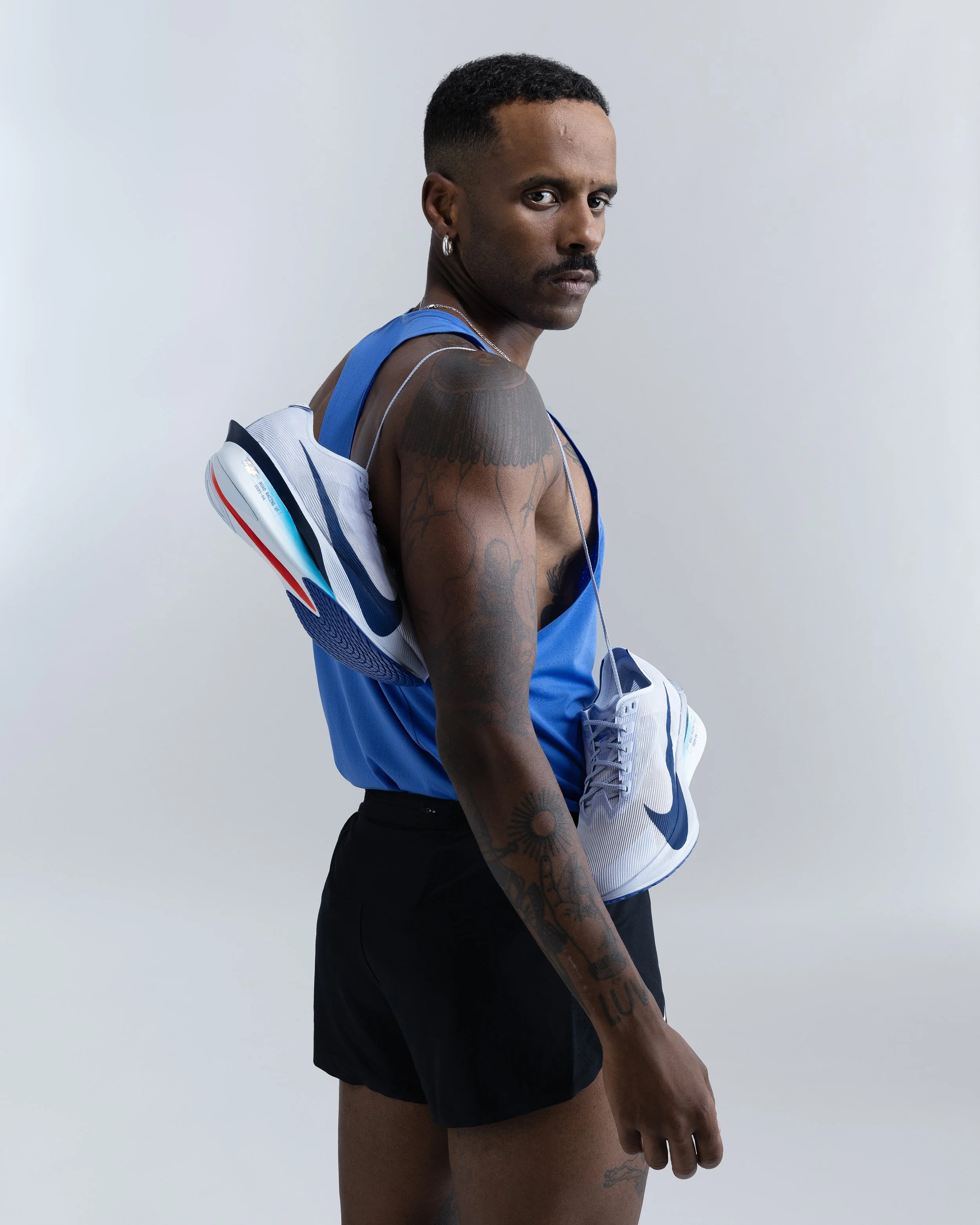 Man dressed in athletic clothing holding Nike shoes, with a serious expression, against a plain background.