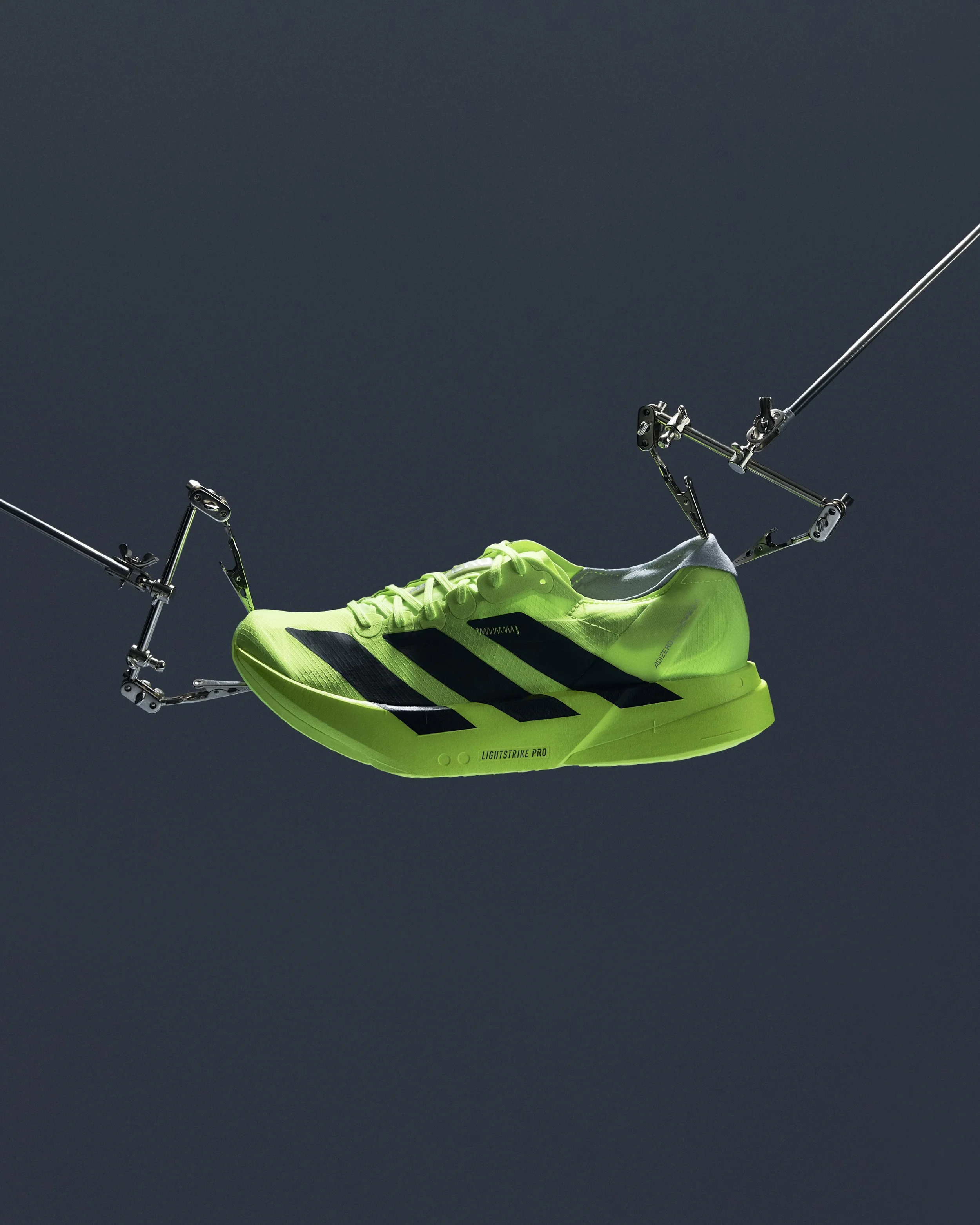 A bright green running shoe suspended by mechanical arms against a dark background.