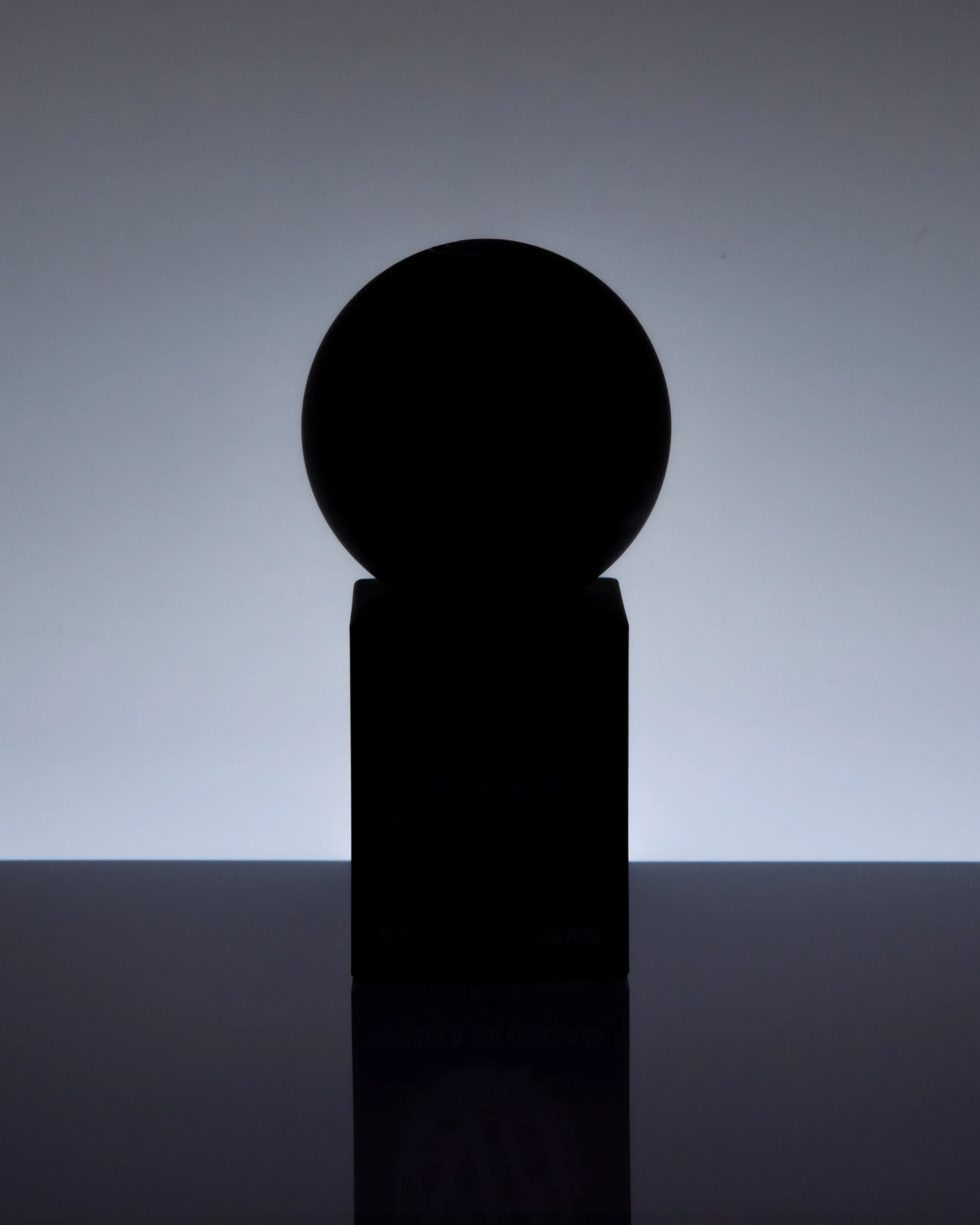 Silhouette of a spherical object on a rectangular stand against a gradient background.
