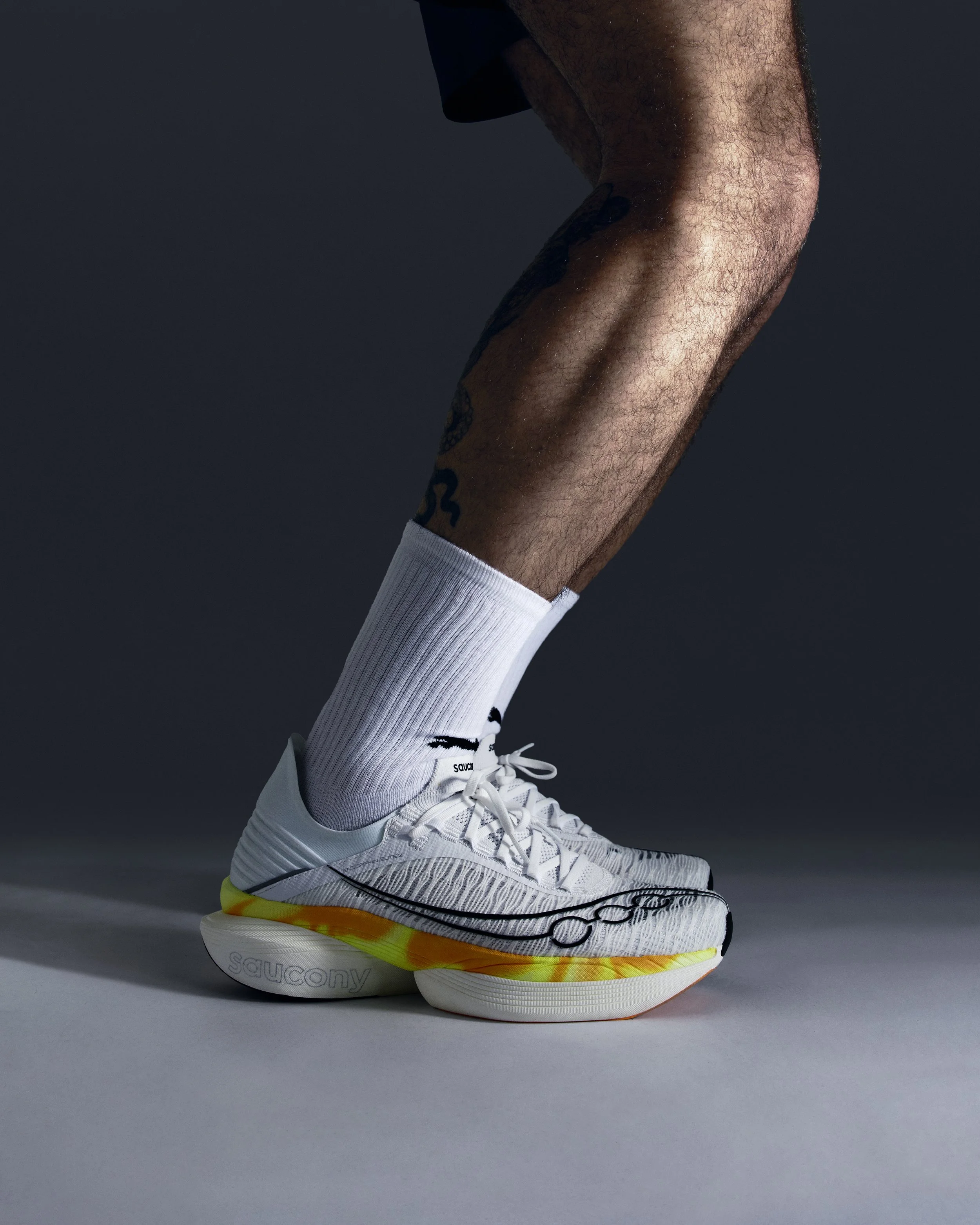 Close-up of a man's legs in white athletic shoes and socks, against a dark background.