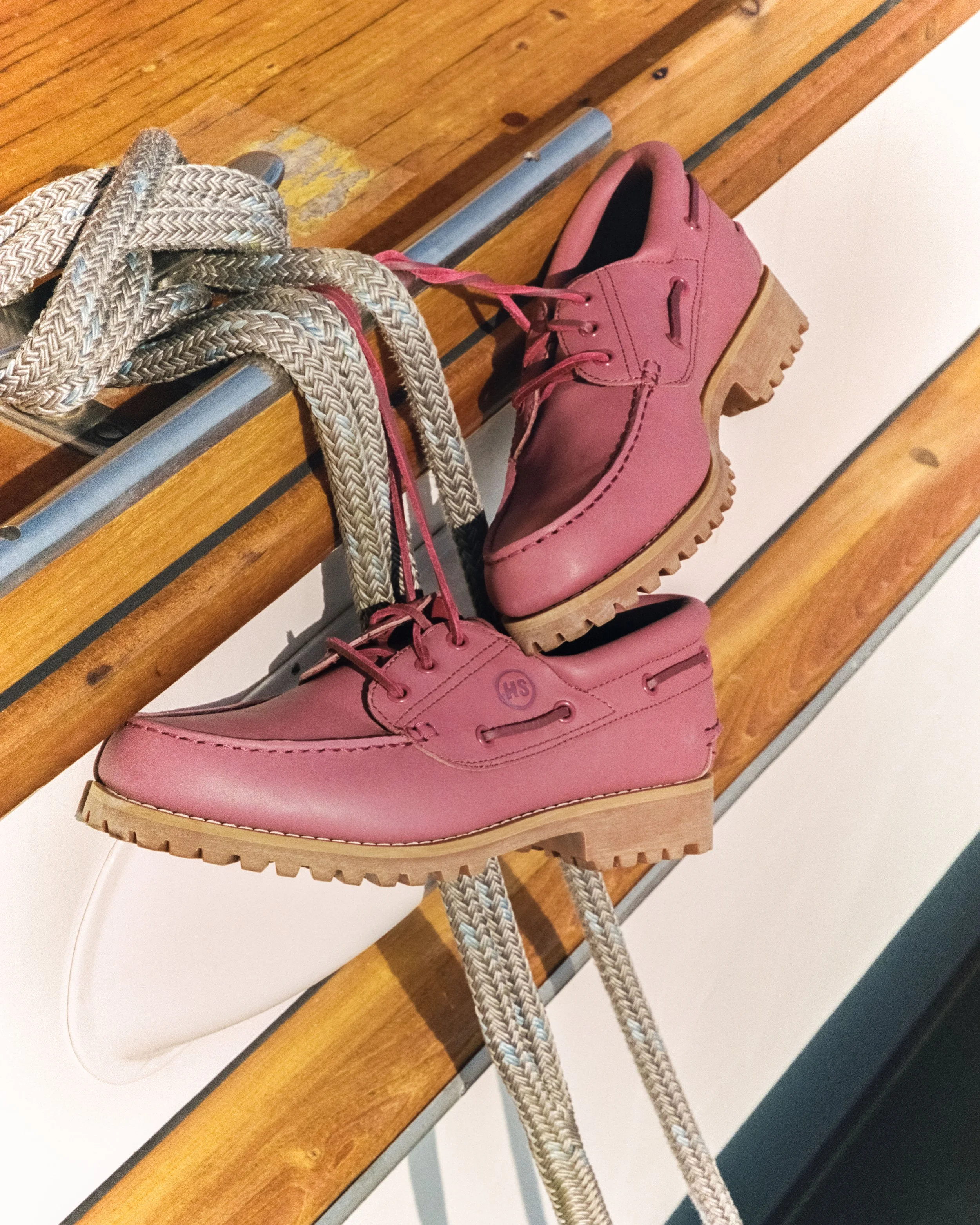 Pink leather shoes with chunky heels and gray and white shoelaces resting on a wooden bench.