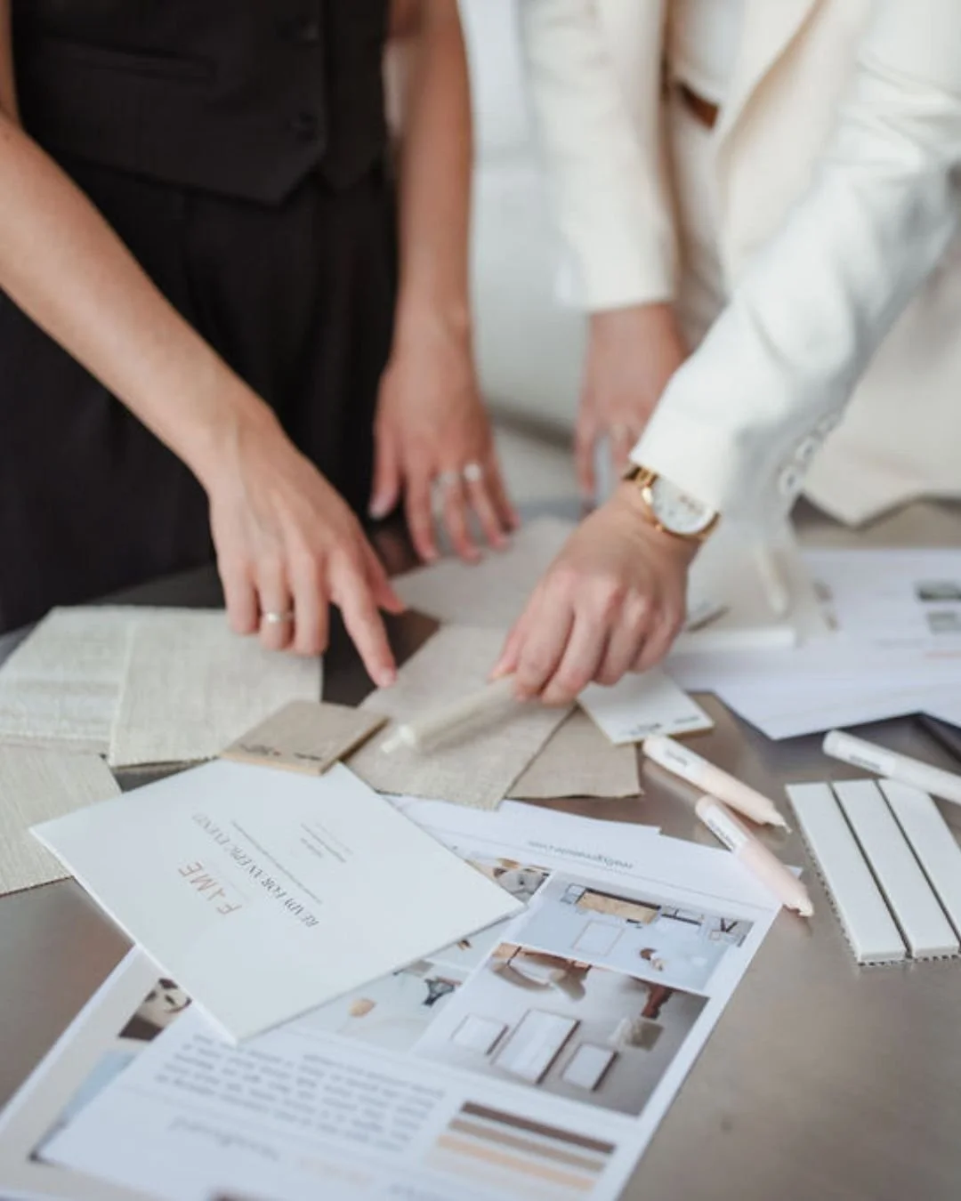 Two people reviewing fabric and interior design samples at a table, surrounded by printed interior design materials and color swatches.