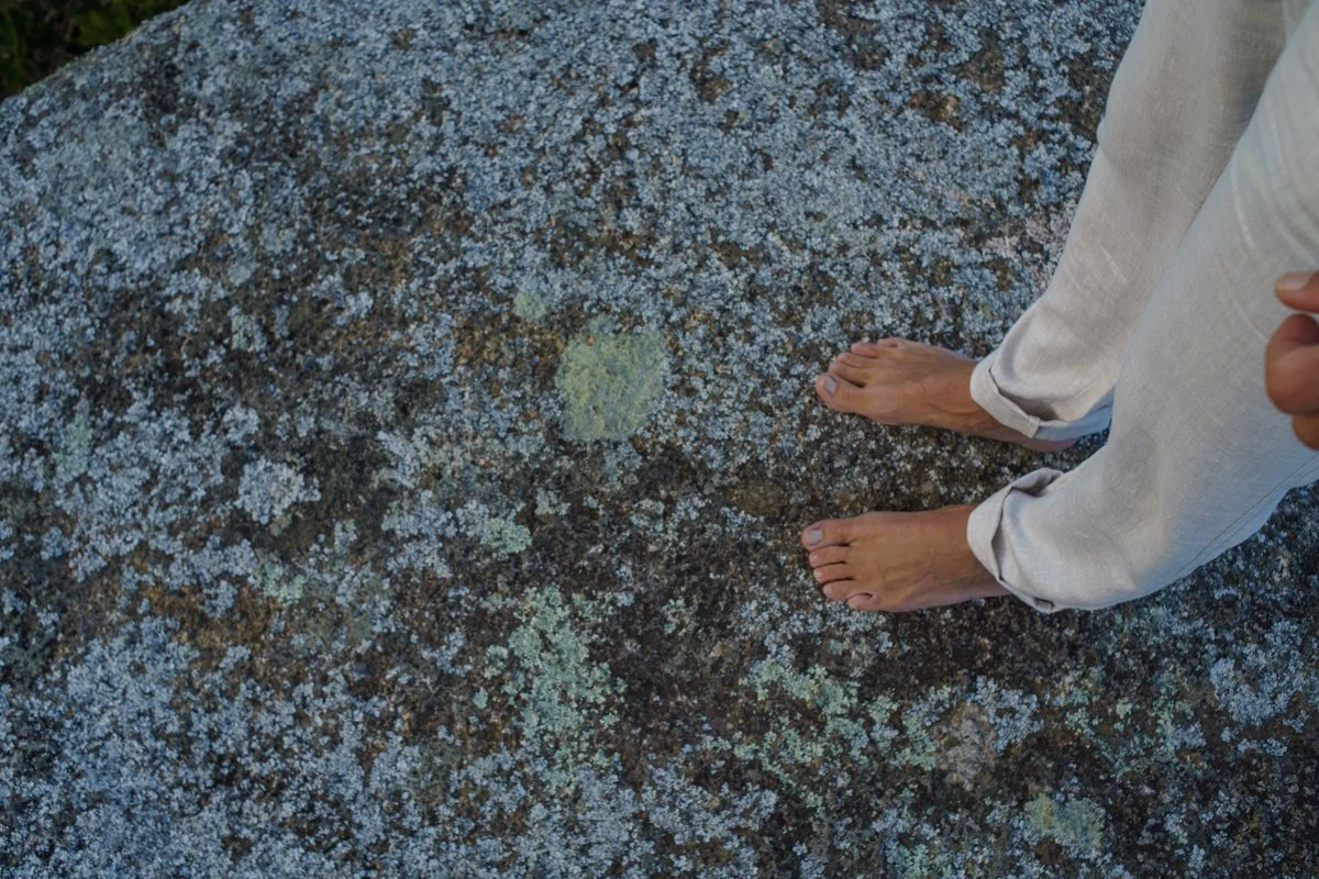 Pies descalzos sobre rocas cubiertas de musgo y líquenes de color verde y gris.