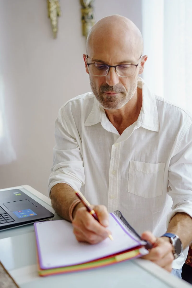 Hombre calvo con gafas escribiendo en una libreta en un ambiente de oficina