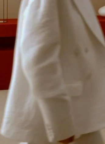 Partial view of a person wearing a white coat or blazer, with a red background.