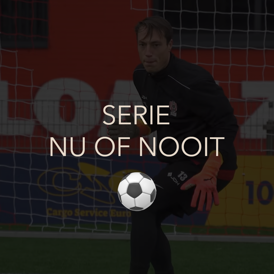 Soccer goalkeeper in black uniform with orange gloves standing in front of a goal net inside a sports arena.