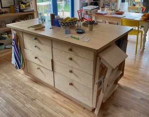 Wooden kitchen island with six drawers, a folding side shelf, and various items on top, in a bright dining area.