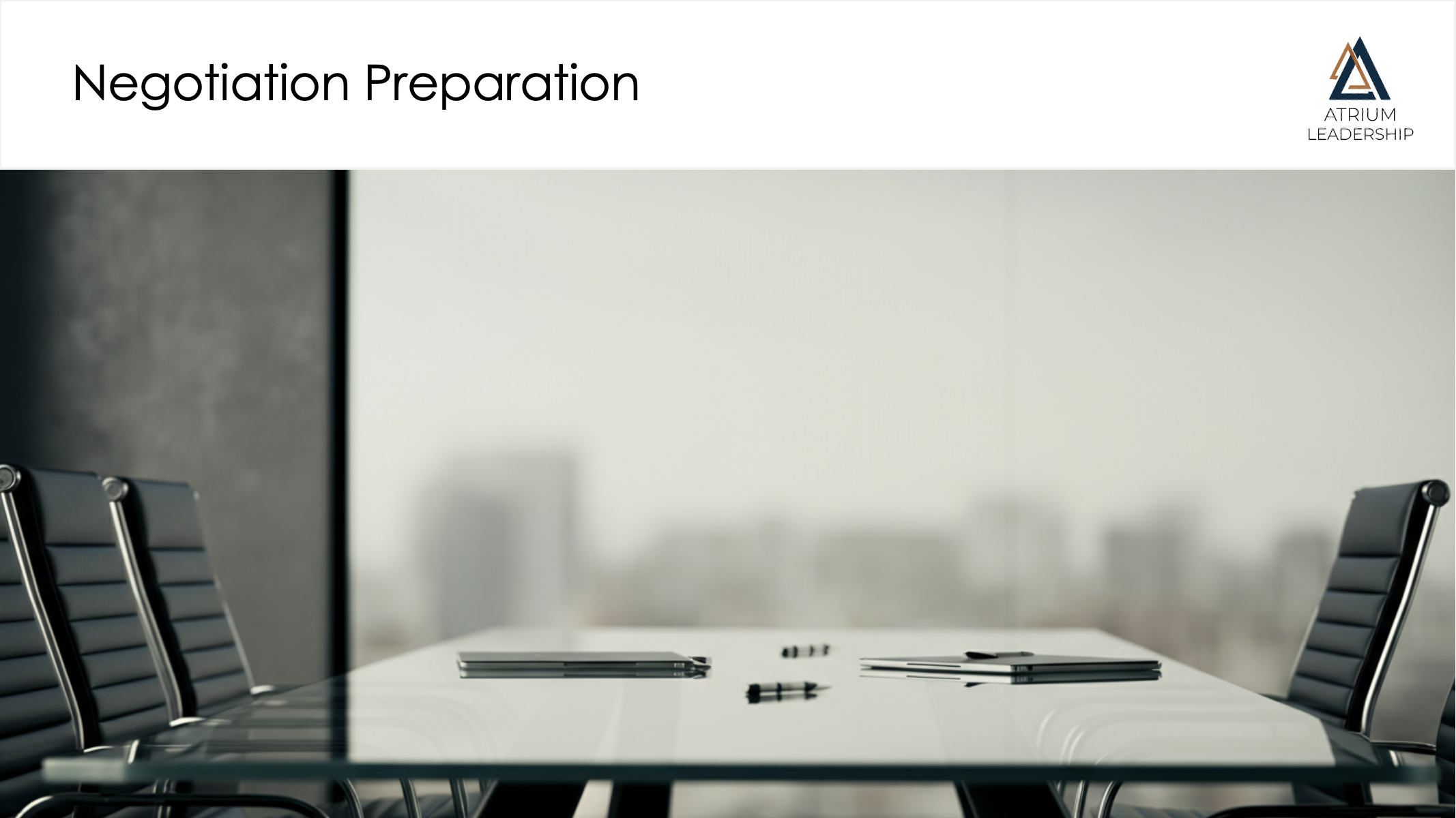Empty conference room with a glass table, three closed laptops, two pens, and four chairs around the table, with a cityscape view outside the window.