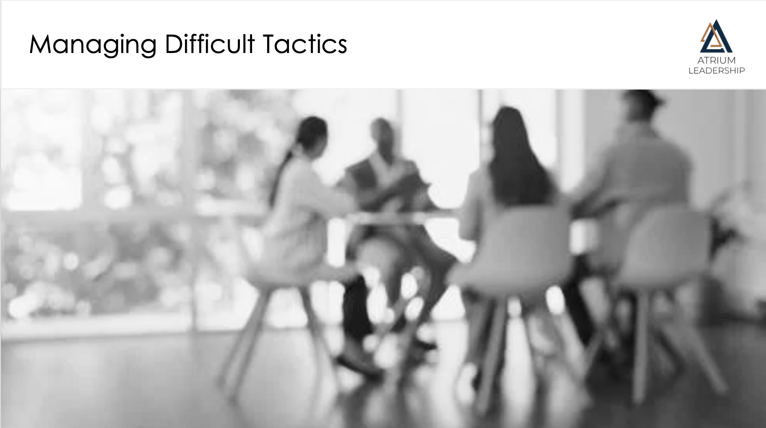 A group of four people sitting around a table in a meeting room, engaging in a discussion. The background shows large windows with a blurred view outside.