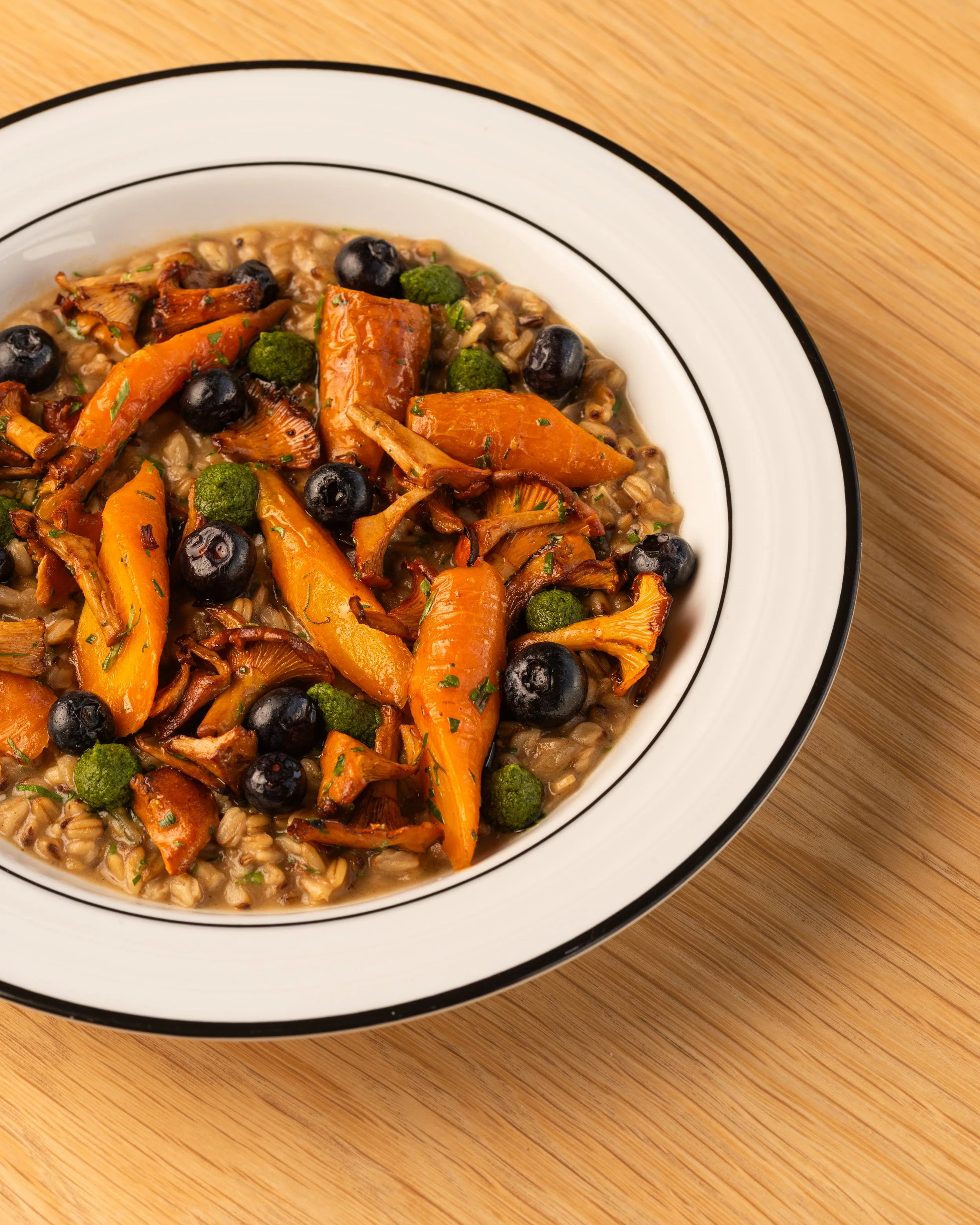 Close-up of a bowl of mushroom and vegetable risotto on a wooden dining table.