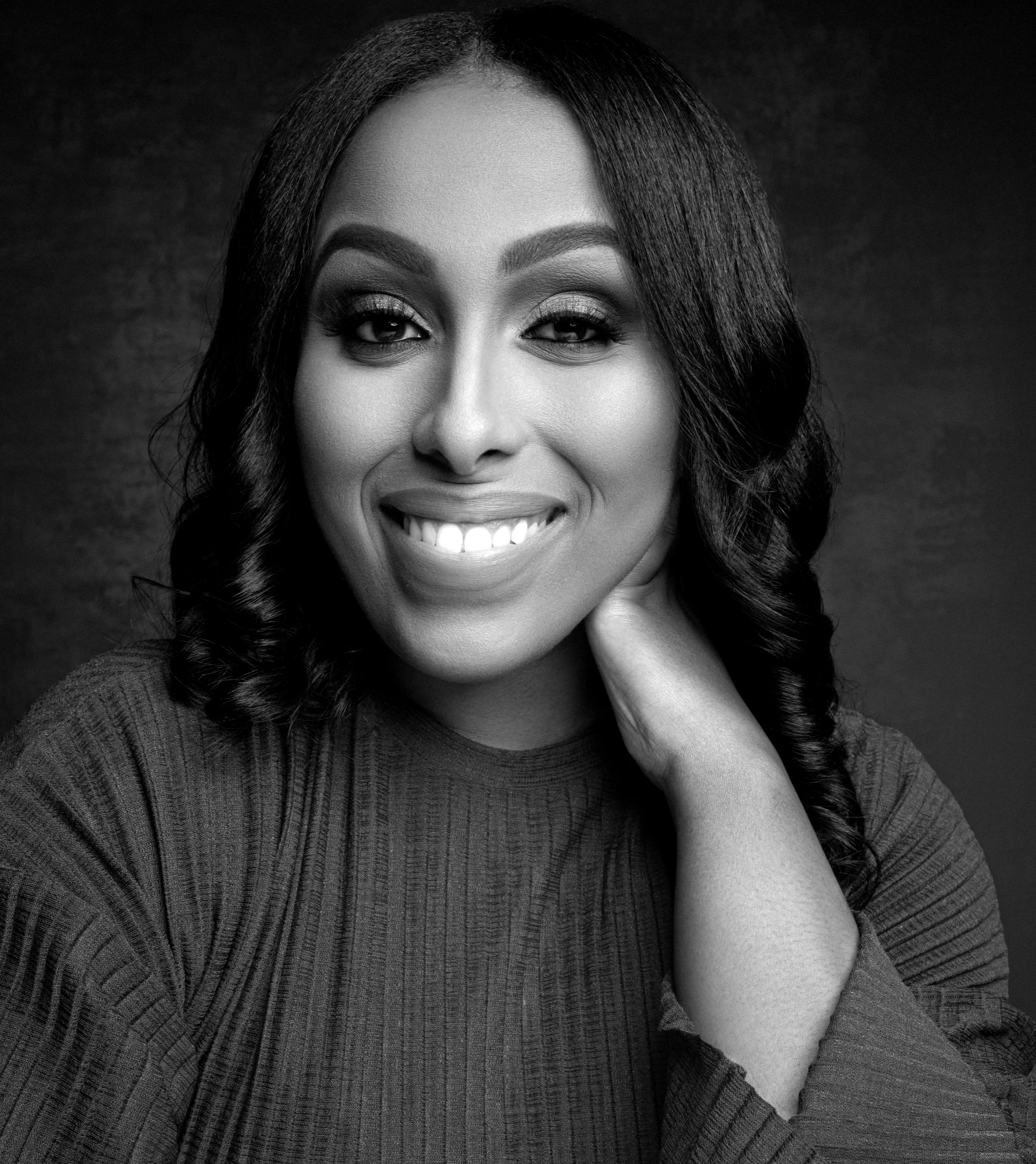 Black and White Photo of Bethel Dixon, film producer facing the camera with a smile and left hand behind her neck/head