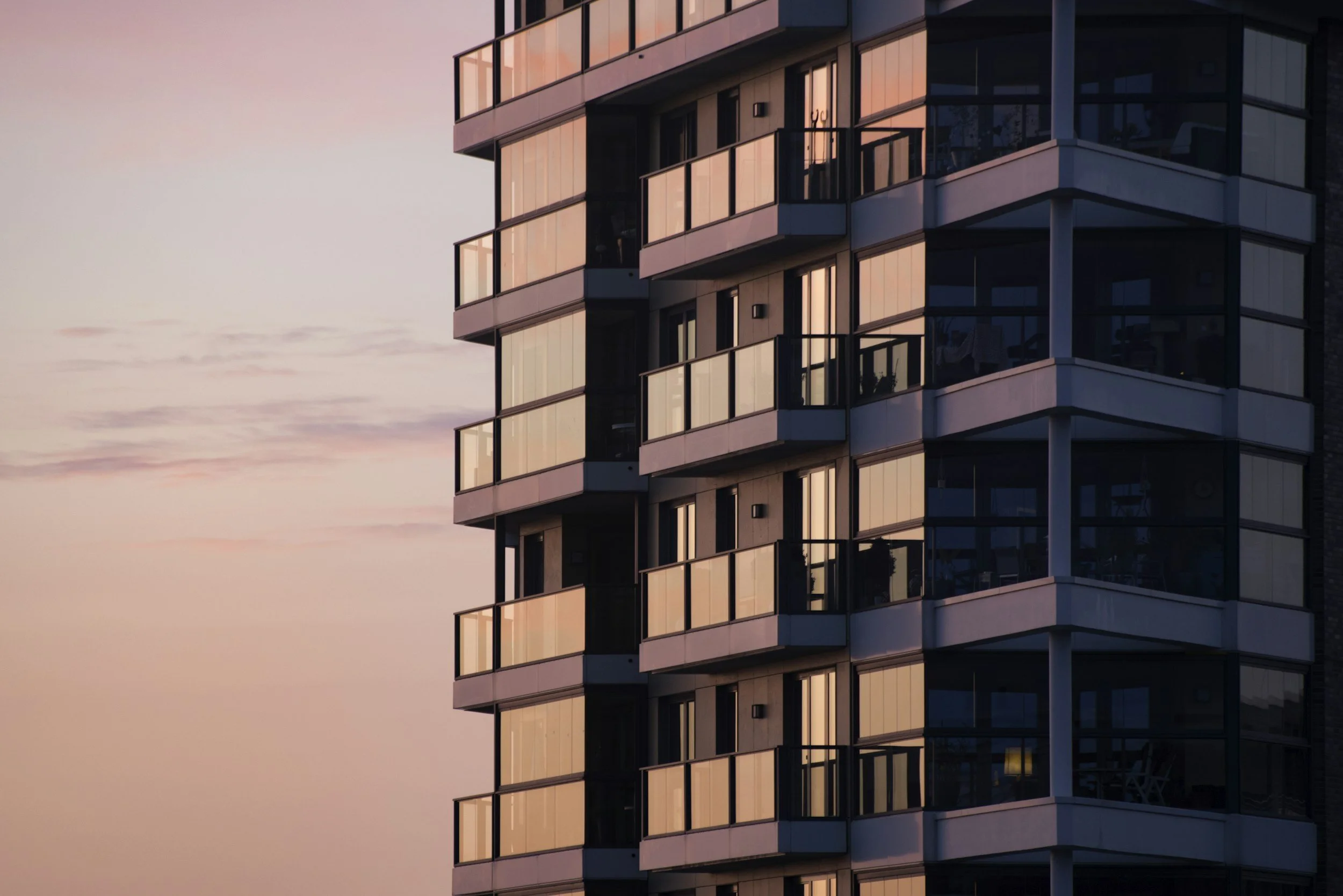 Modern high-rise apartment building with glass balconies reflecting a colorful sunset sky.