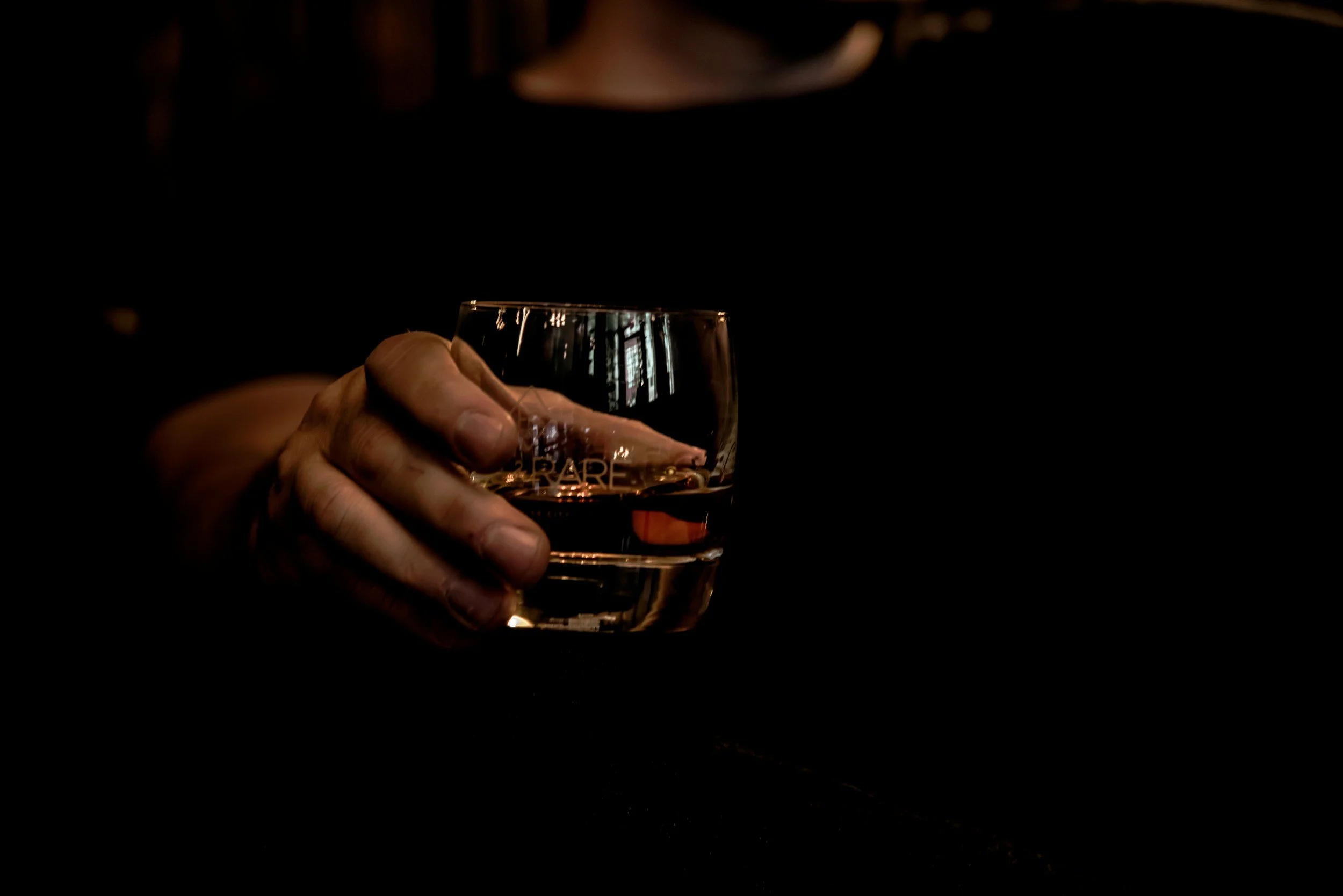 Close-up of a hand holding a glass of whiskey against a dark background.