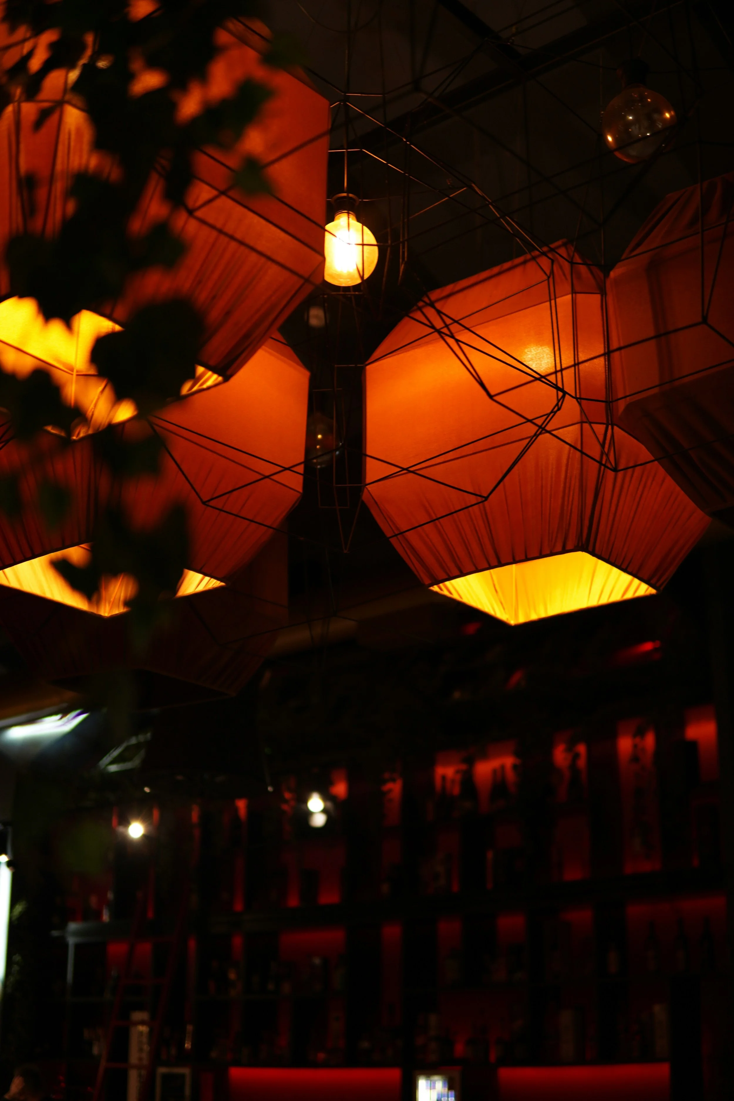 Warm orange lighting fixtures hanging from a dark ceiling in a dimly lit bar or lounge.