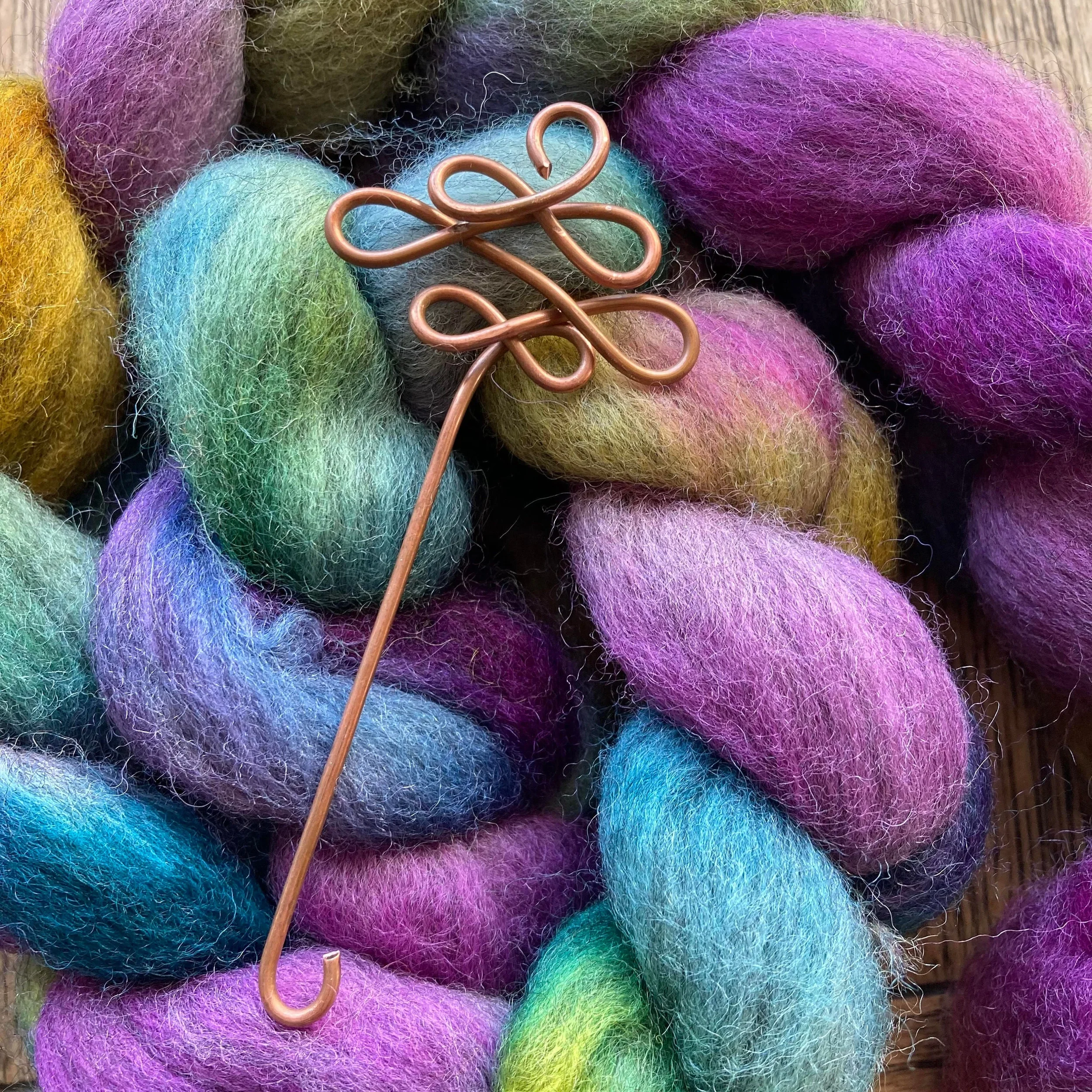 Close-up of colorful felted wool balls in shades of yellow, purple, green, blue, pink, and purple, with a copper wire intertwined among them.