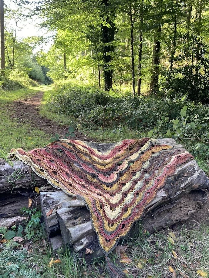 Colorful knitted or crocheted blanket draped over a fallen log in a lush green forest.