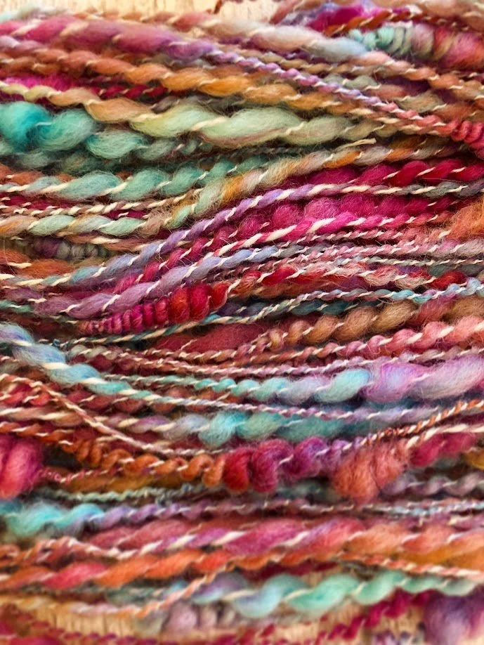 Close-up of multicolored, textured yarns in pink, orange, turquoise, and purple.