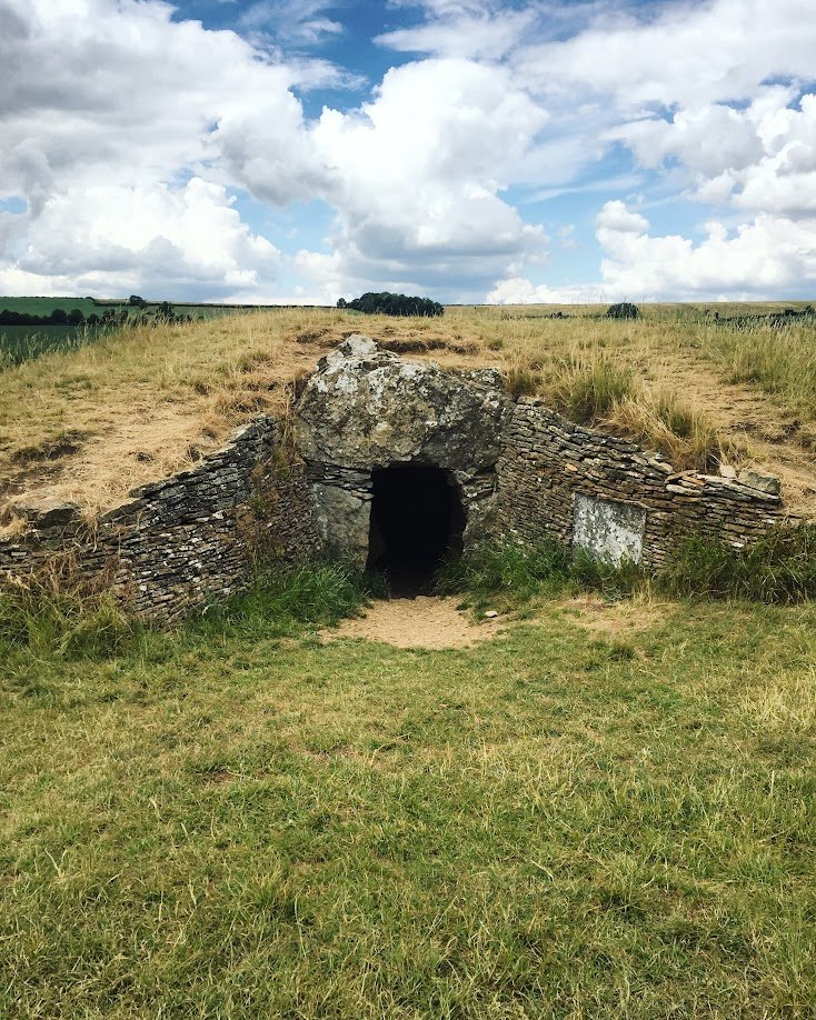 A small stone and brick tunnel entrance in a grassy field with a cloudy sky overhead.