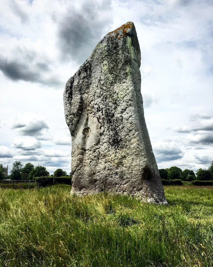 A large, upright stone standing in a grassy field under cloudy skies.
