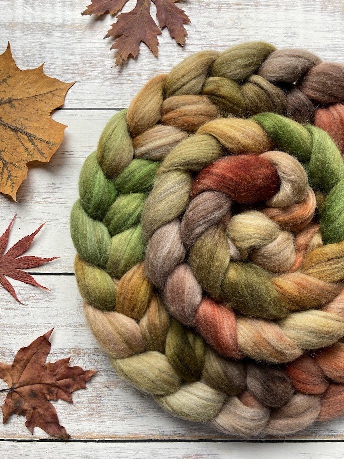 Colorful braided wool yarn with autumn leaves on a white wooden surface.