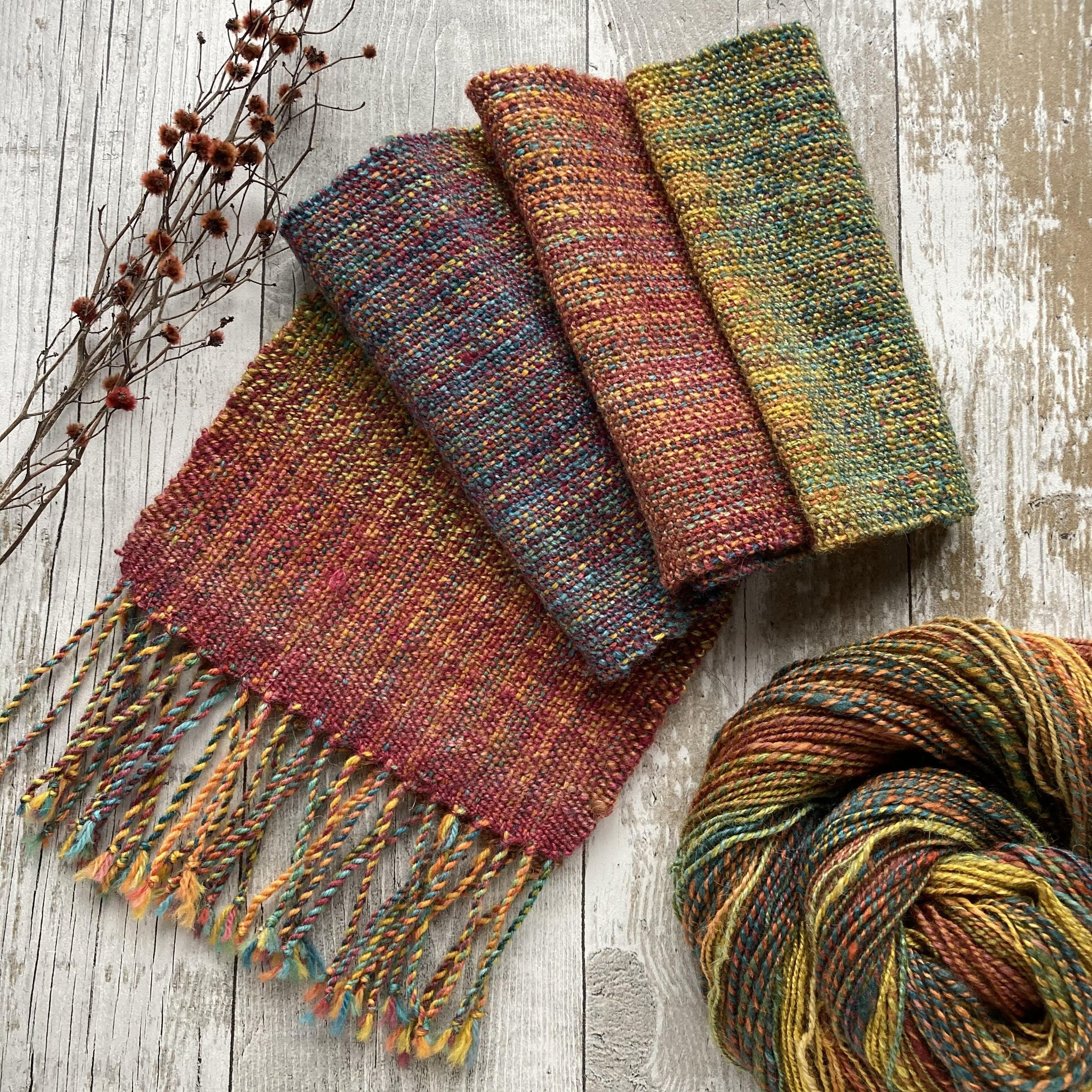 Colorful woven textiles and dried brown plant branches on a wooden surface.