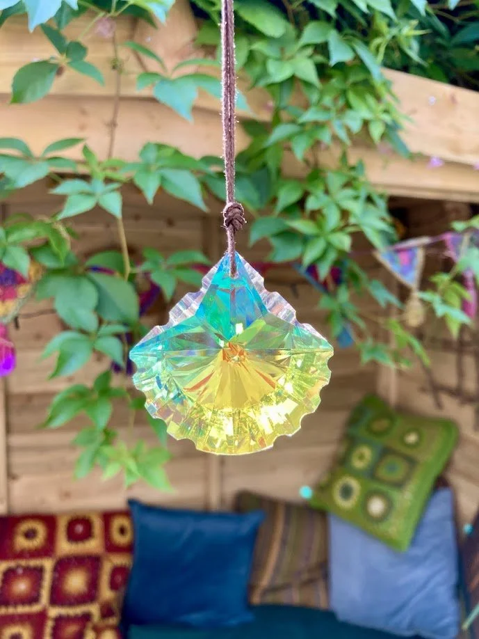 A crystal ornament hanging from a string in a garden with green plants and a wooden fence in the background.