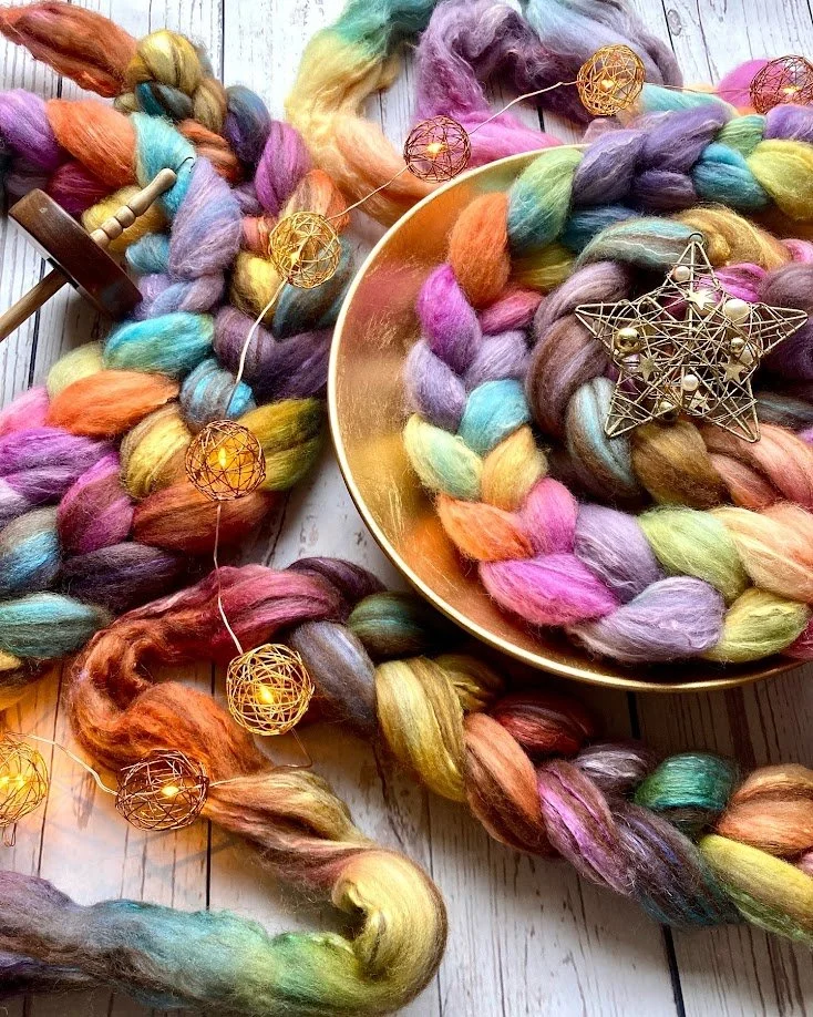 Colorful, thick yarn braids with pastel and earth tones, decorated with warm white string lights, a golden bowl, and metallic star-shaped ornament on a wooden surface.