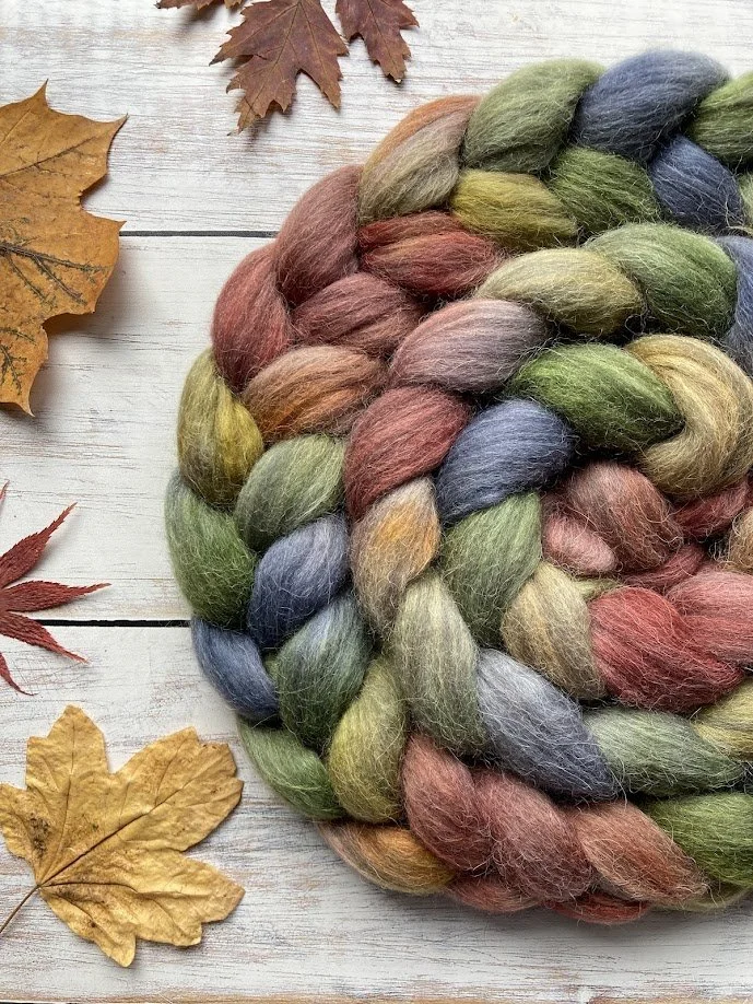 Colorful braided wool yarn on white wooden surface with autumn leaves around it.