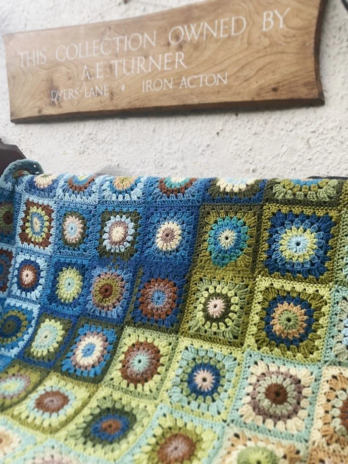Colorful crocheted blanket with granny square pattern hanging on wall.