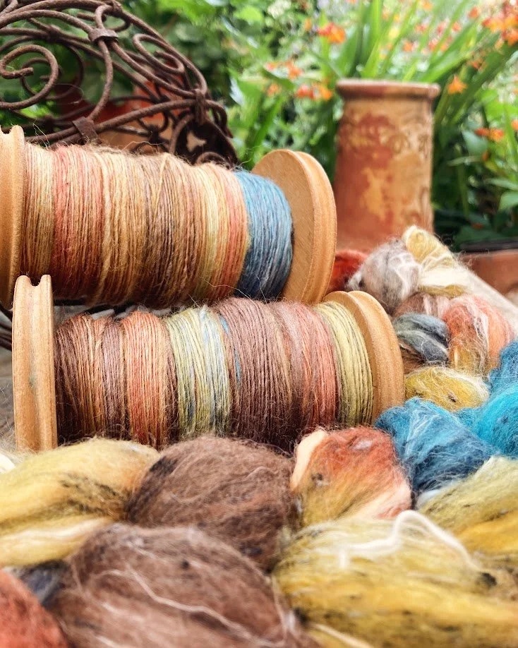 Spools of multicolored yarn and wool fibers outdoors using ceramic pots and garden plants.