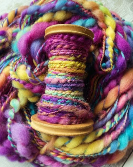 Close-up of a spool of multicolored yarn surrounded by various other colorful yarn strands.