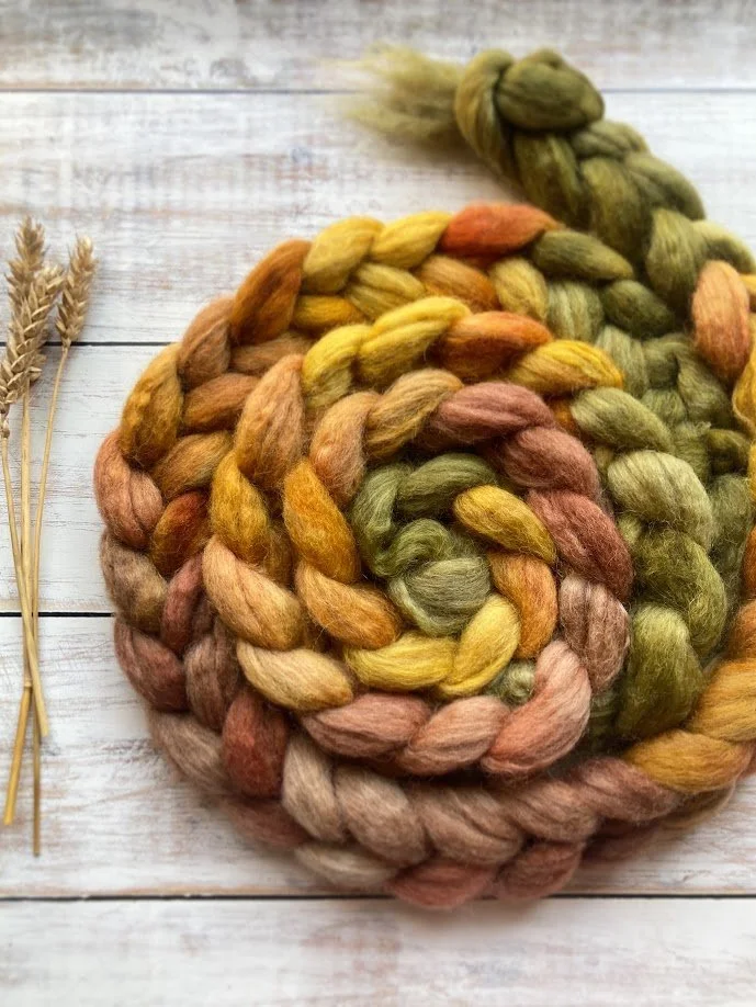 Colorful braided wool balls placed on a white rustic wooden surface, with dried wheat stalks on the side.