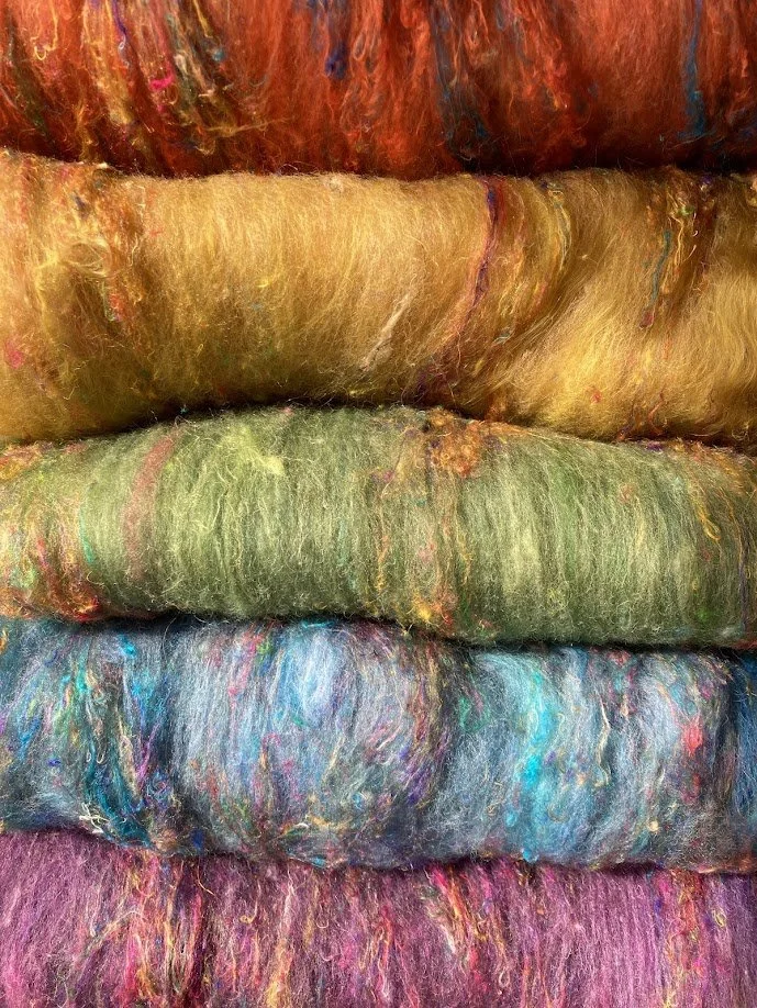 Stacked colorful felted wool yarns in shades of red, yellow, green, blue, and purple.