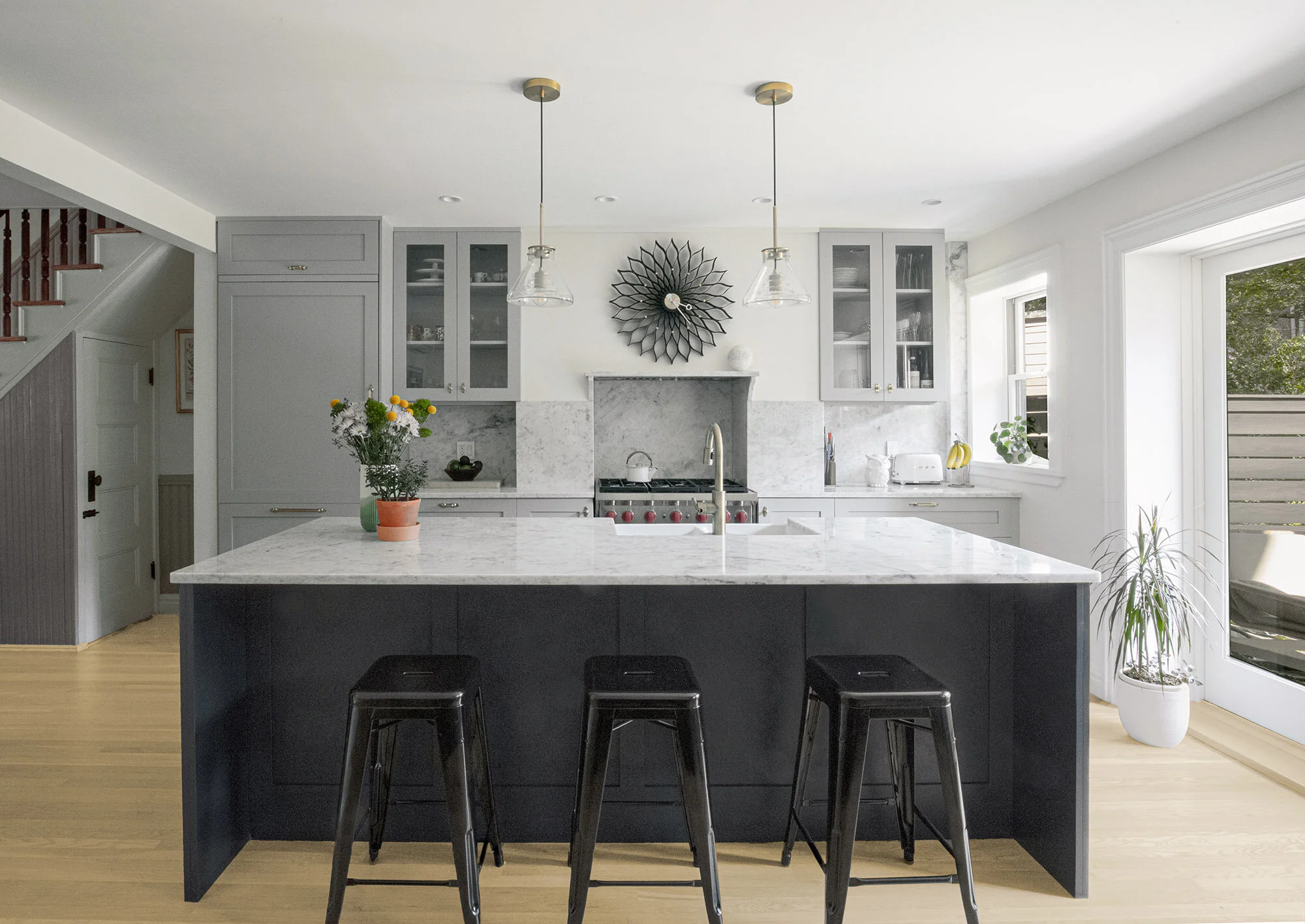 Modern kitchen with gray cabinets, marble countertop island, black stools, stainless steel appliances, pendant lights, and decorative wall art.