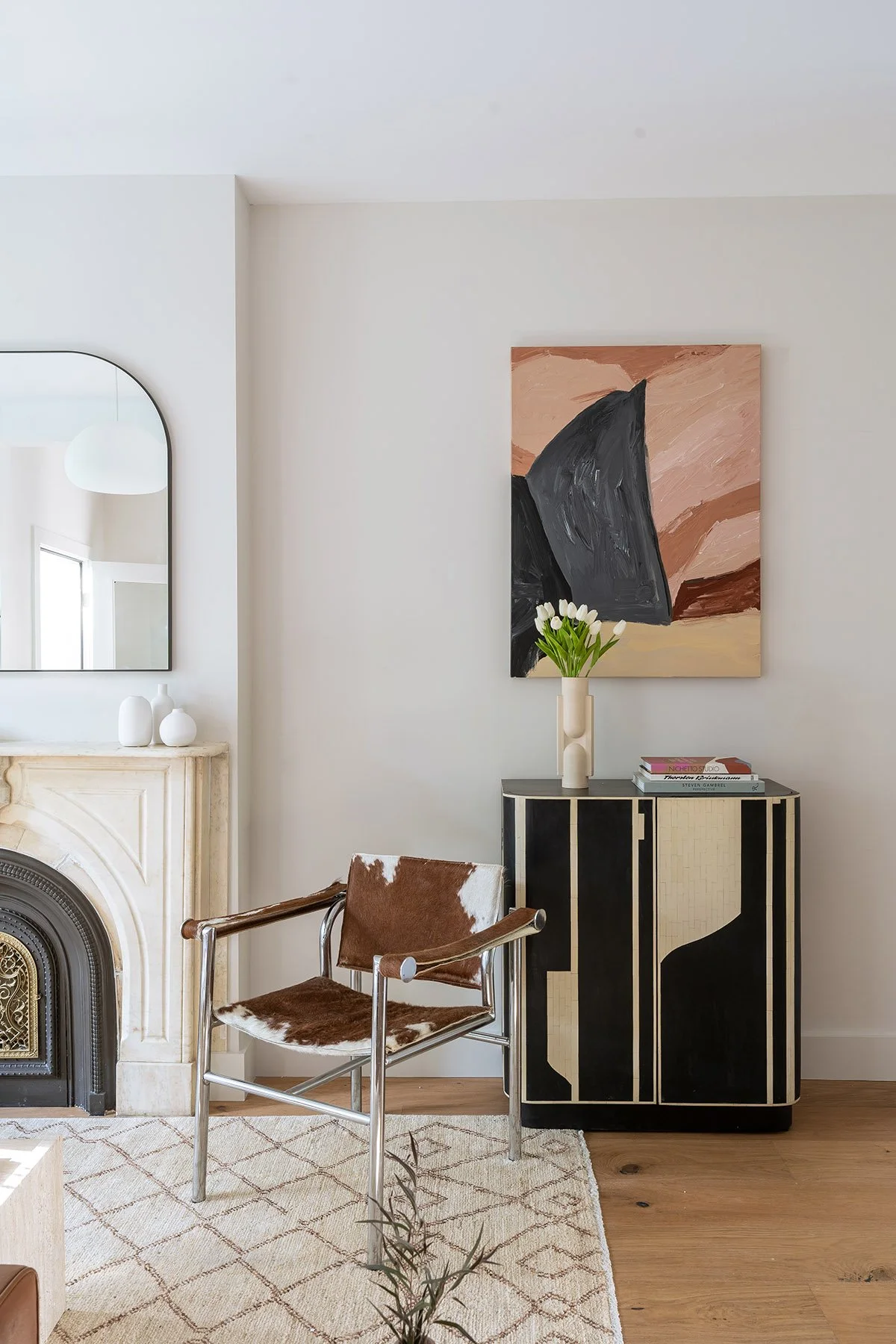 Modern living room with a cowhide chair, abstract painting, decorative cabinet, white fireplace, and geometric rug.