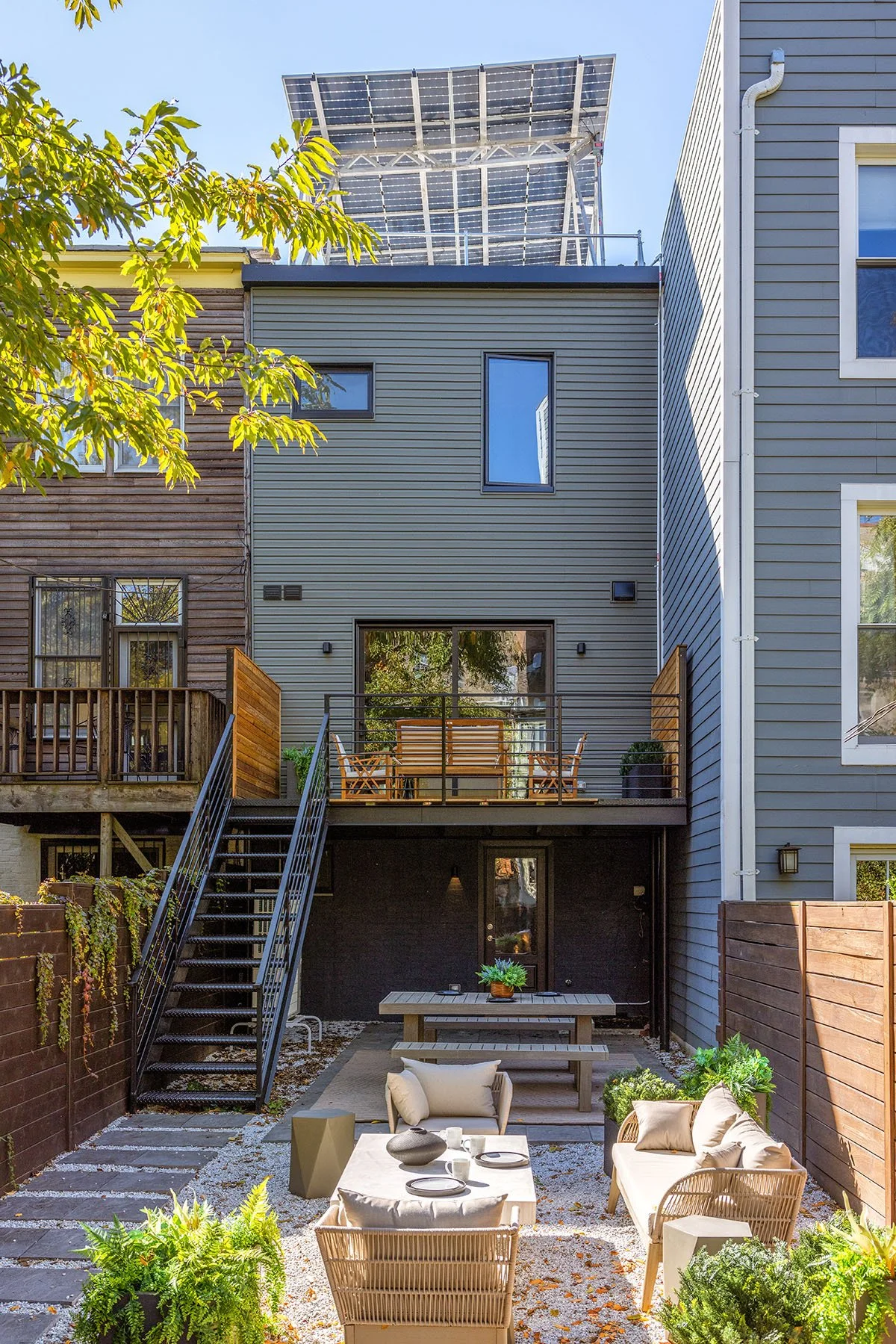 Modern backyard renovation with outdoor seating and dining area, wooden fence, and rooftop solar panels.