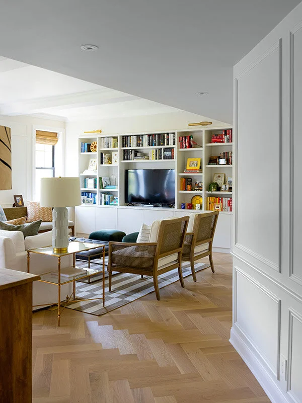 Modern living room with built-in shelves, TV, sofas, and chairs on a parquet floor.