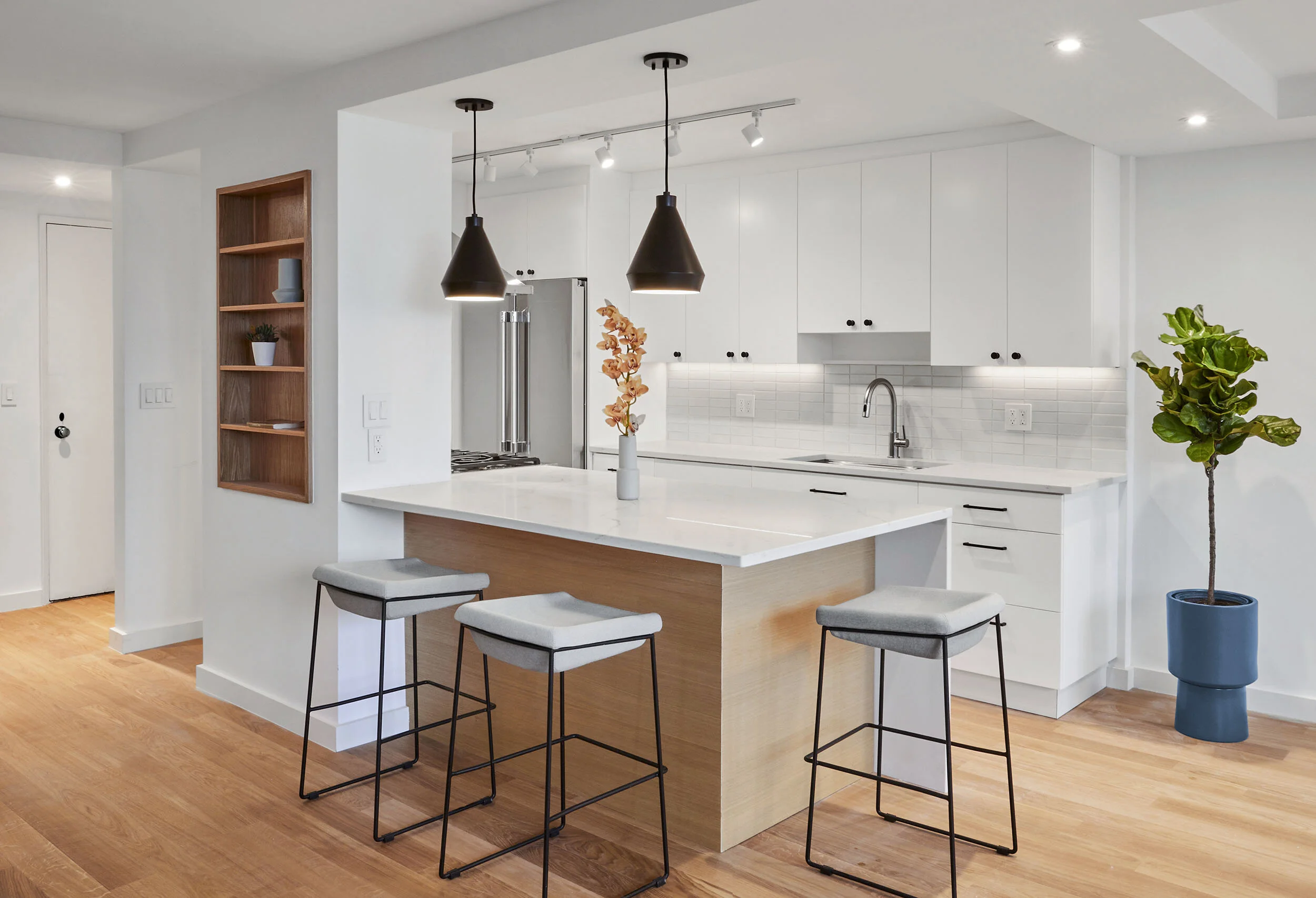 Modern kitchen with white cabinets, island with bar stools, pendant lights, and wooden flooring.