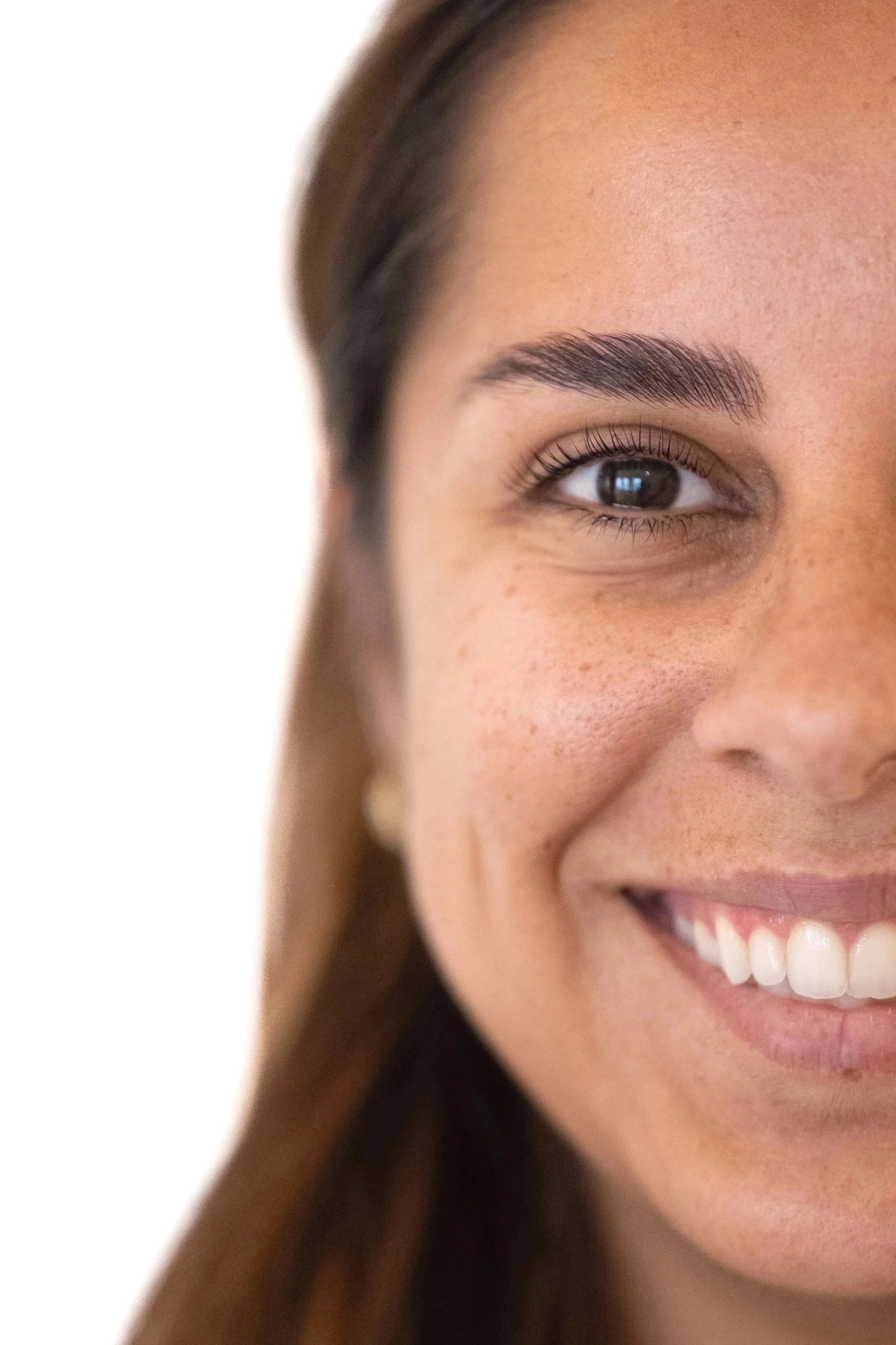 Zoom stylistique sur une femme souriante, montrant ses dents blanches, avec un teint clair, des sourcils épais. avant après d'un recourbement de cils et brow lift.