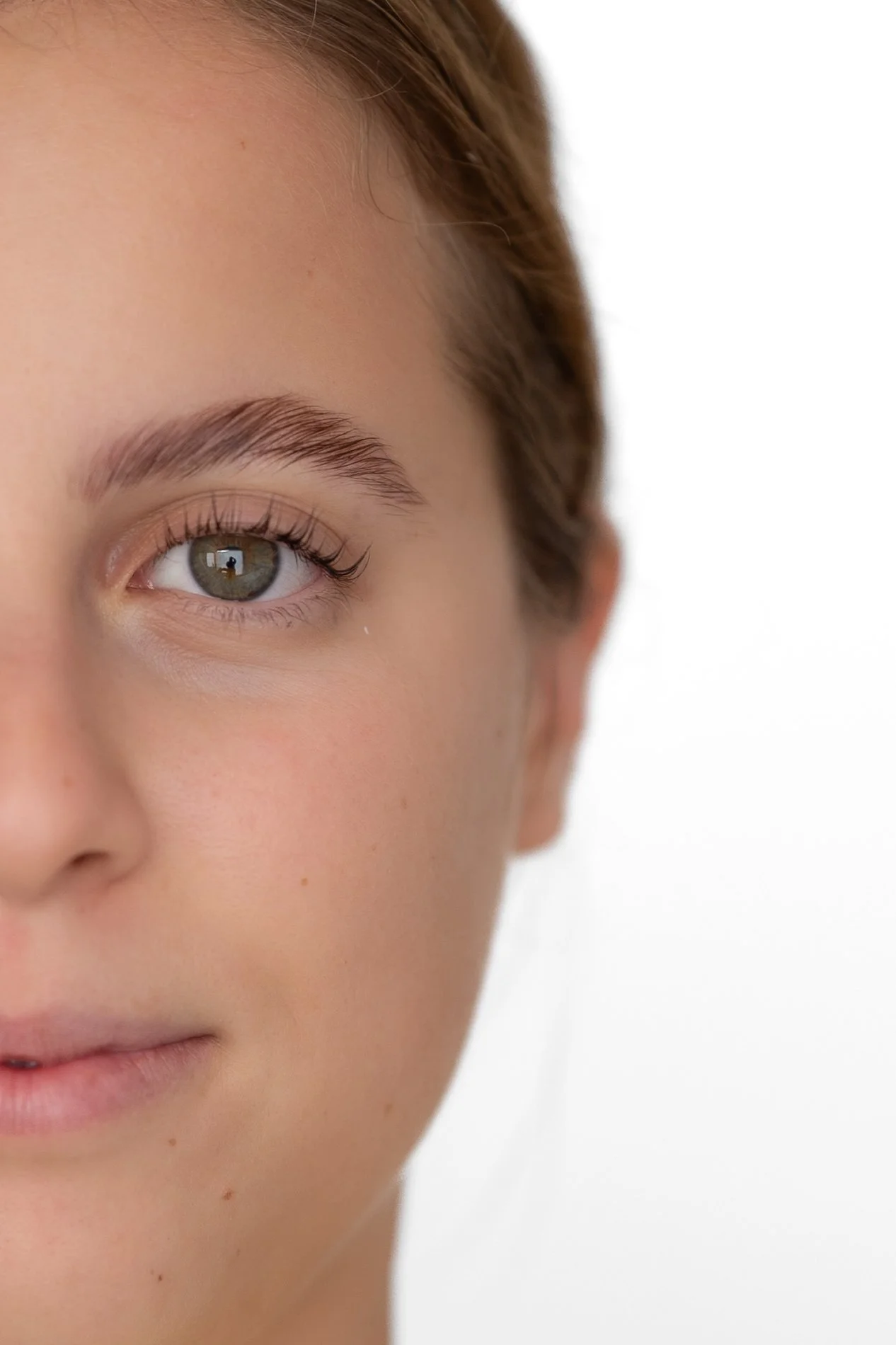 Portrait d'une jeune femme aux yeux verts, peau claire, lèvres légèrement pleines, avec un fond blanc. avant après d'un recourbement de cils et brow lift.