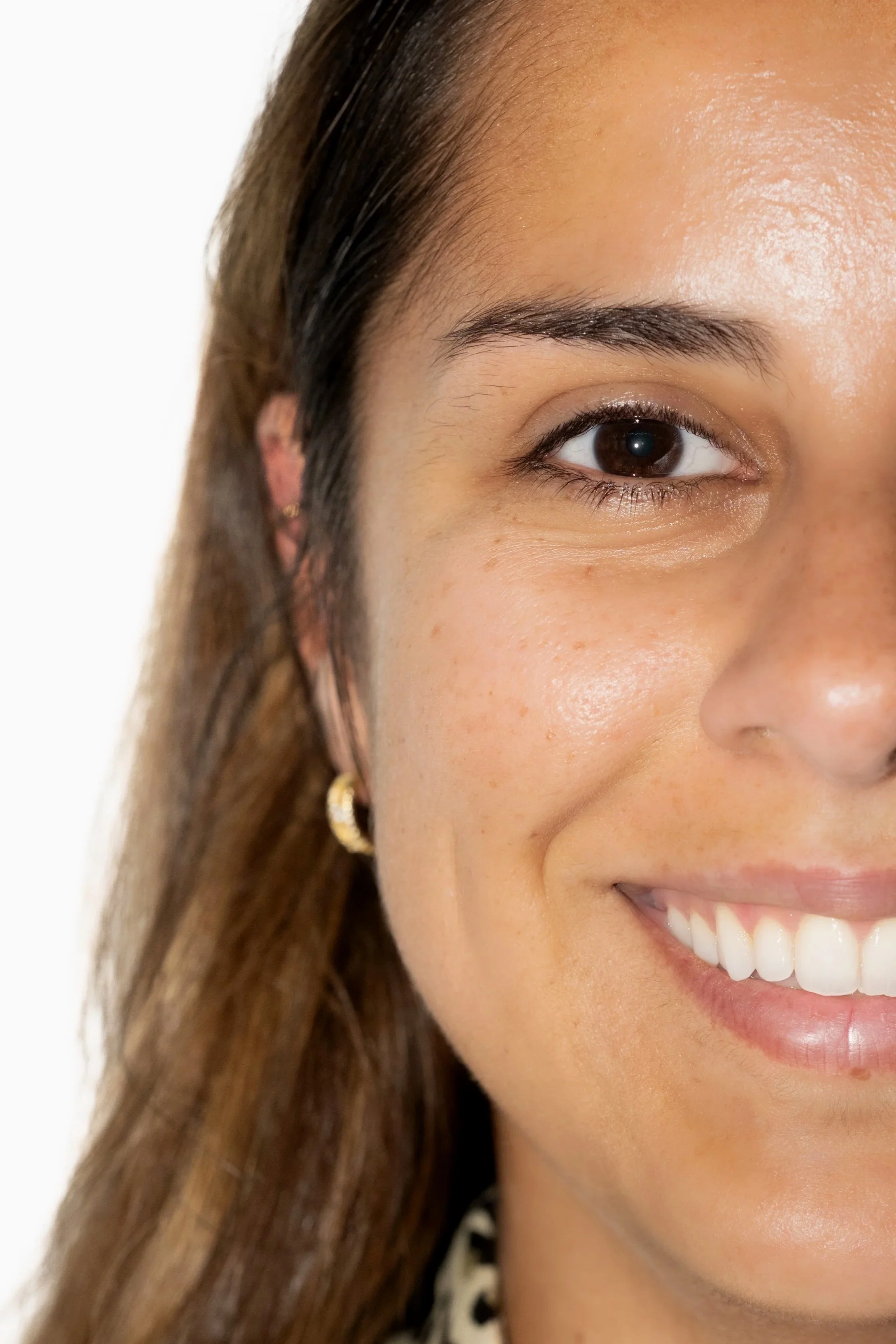 Close-up d'une femme souriante avec une peau claire, des cheveux bruns et des boucles d'oreilles dorées, avant après d'un recourbement de cils et brow lift.