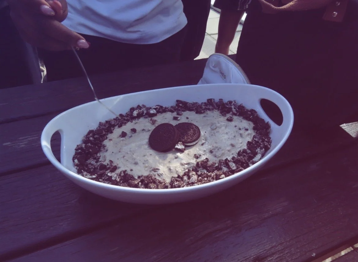 tiramisu dans un plat blanc, avec des Oreo et des morceaux de biscuits autour, sur une table en bois