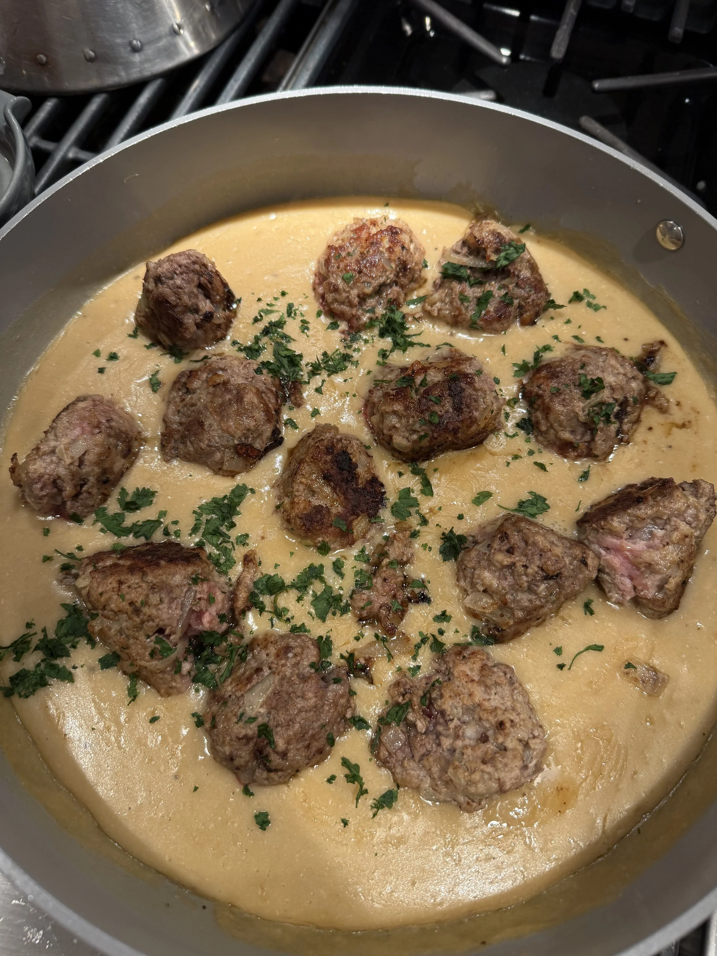 Cooking meatballs in a creamy sauce topped with chopped parsley in a frying pan.