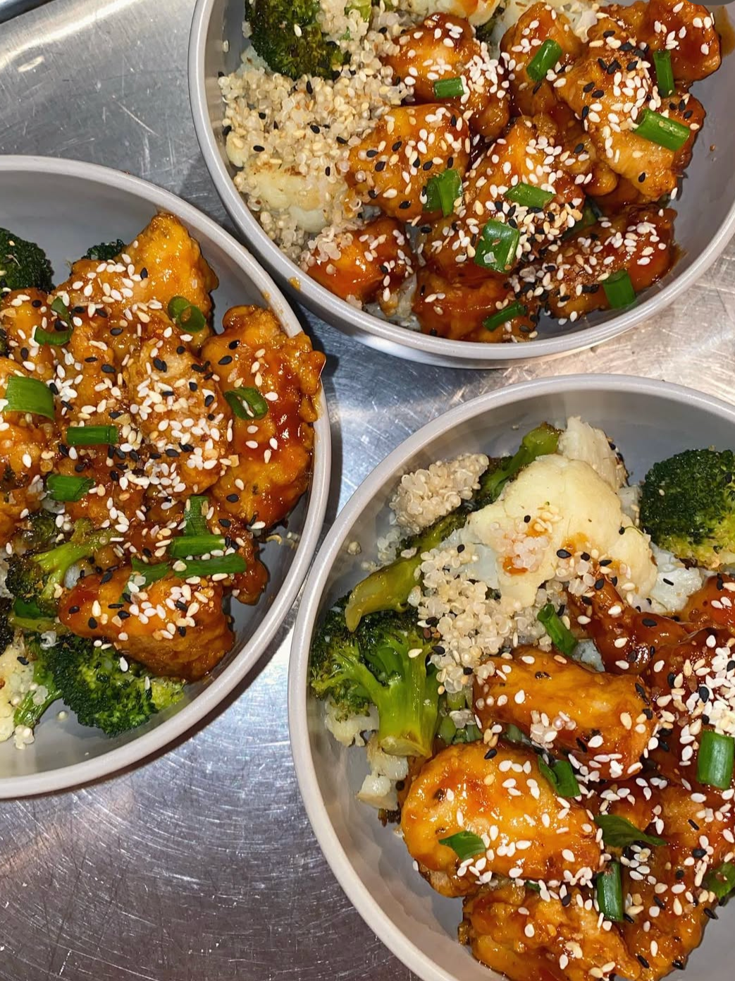 Three bowls of Asian-style chicken and vegetable stir-fry with sesame seeds and chopped green onions over rice.