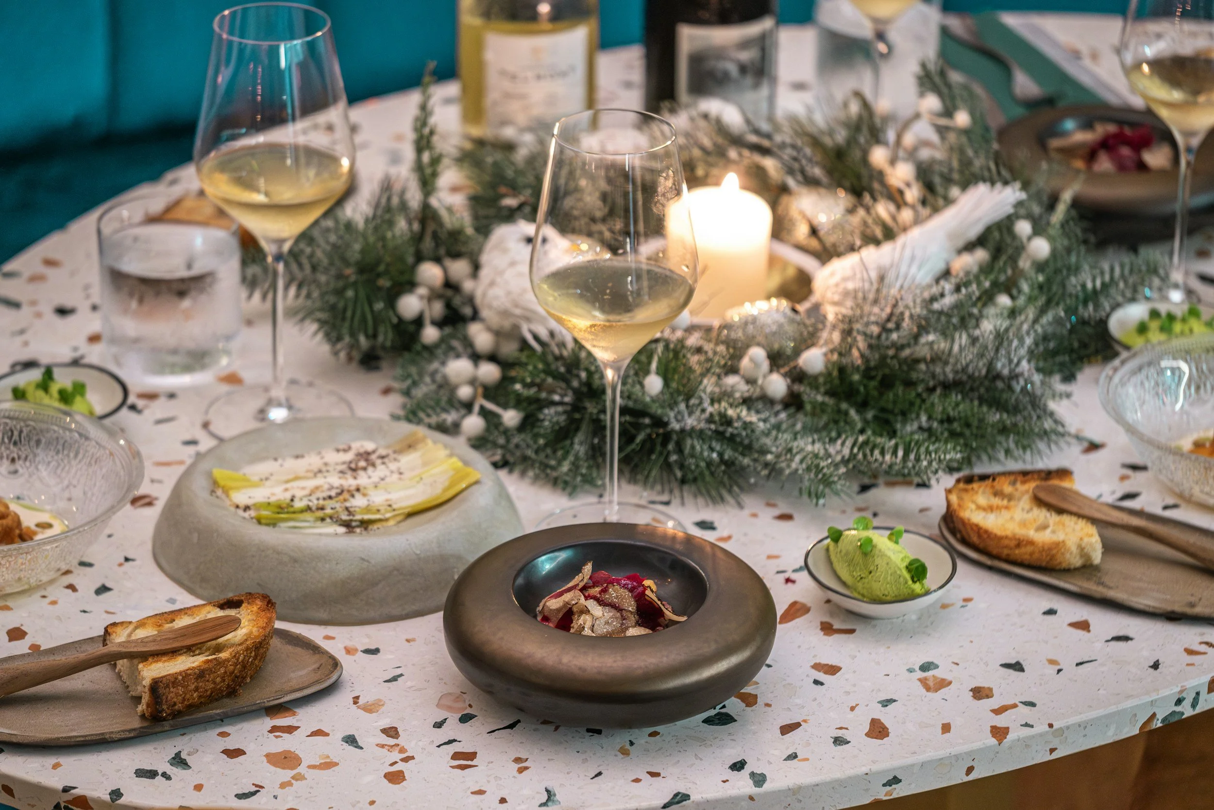 A festive dining table decorated with a candle centerpiece and assorted dishes, including wine glasses, green mousse, bread, and various appetizers.