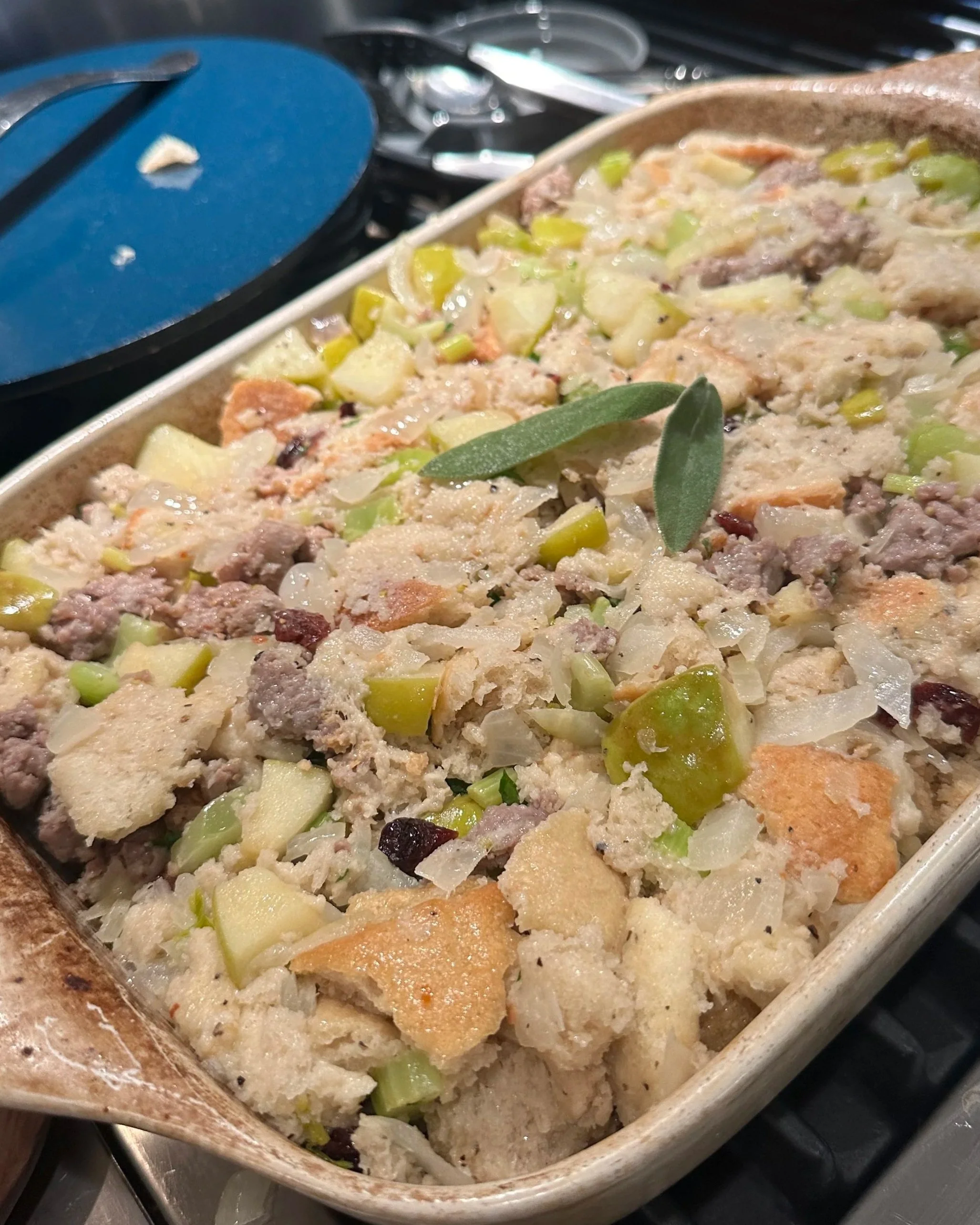 A casserole dish filled with a mixed meat and vegetable dish, topped with herbs.