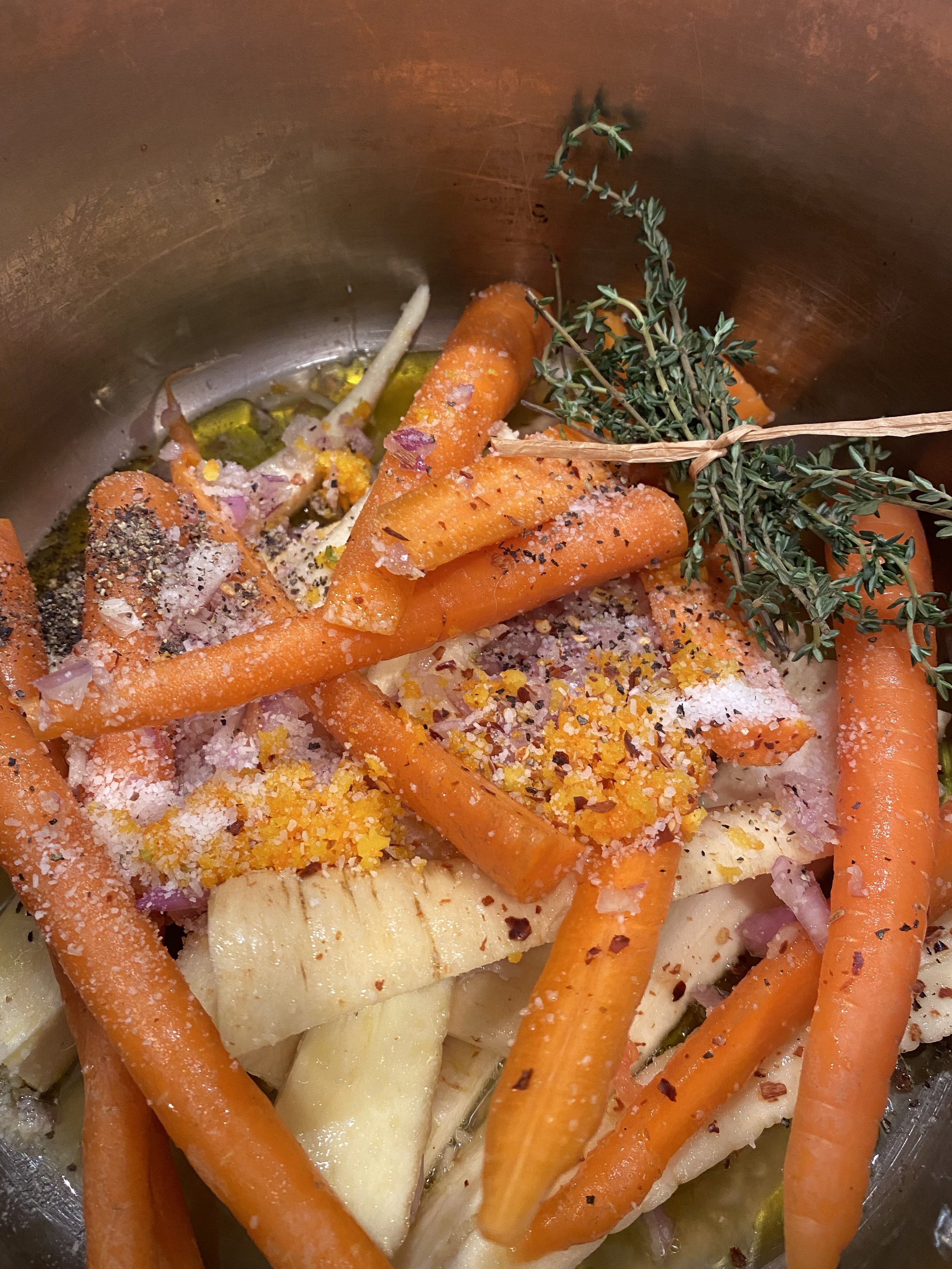 Raw carrots, parsnips, and onions in a pot with herbs and spices, including thyme and pepper, ready for cooking.