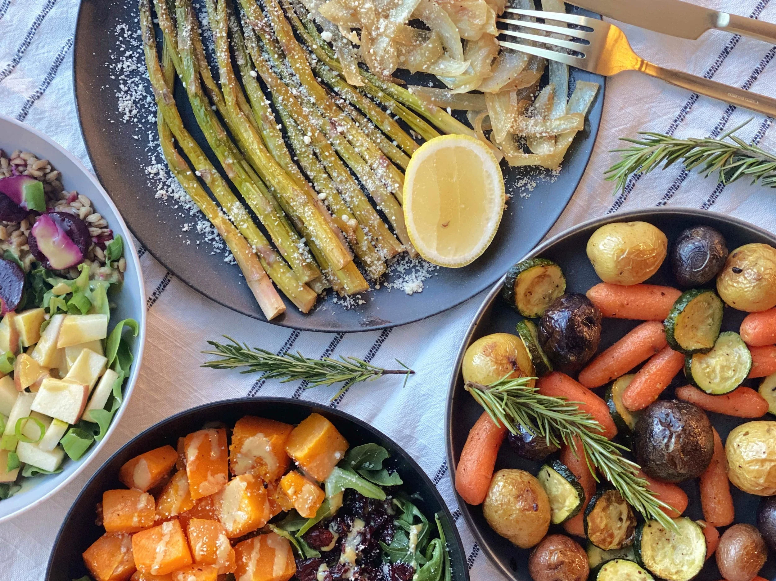 A flat lay of a meal with roasted vegetables including carrots, baby potatoes, and zucchini, grilled green onions, and a salad with beets, greens, and cheese.