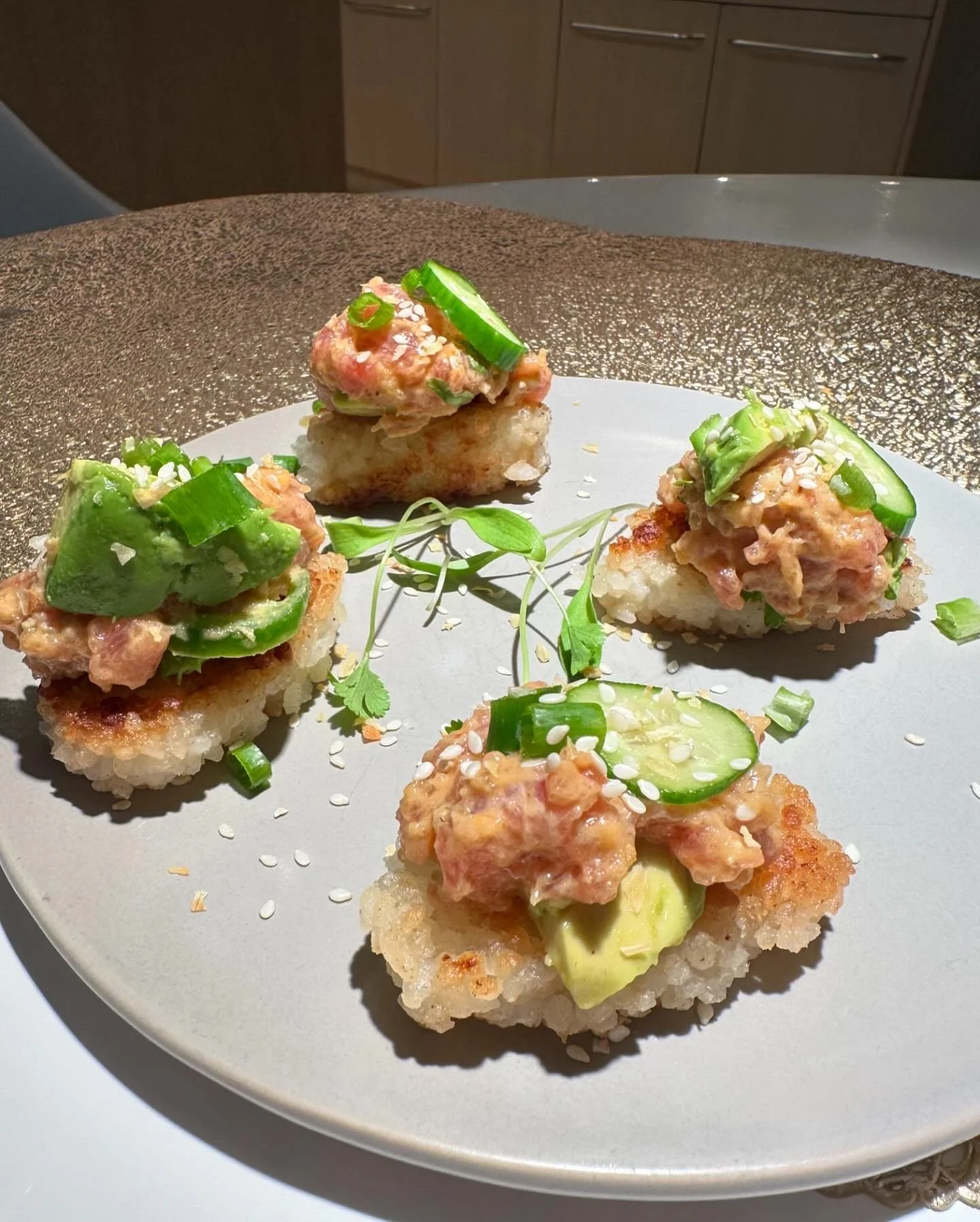 Four pieces of sushi with rice, tuna, cucumber, and green onions, garnished with sesame seeds and microgreens, on a white plate.