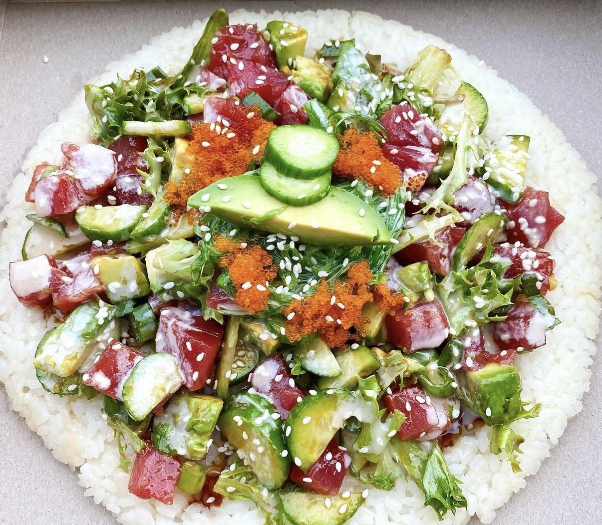 A plate of poke with diced tuna, cucumber, avocado, seaweed, tobiko, and sesame seeds on a bed of rice.